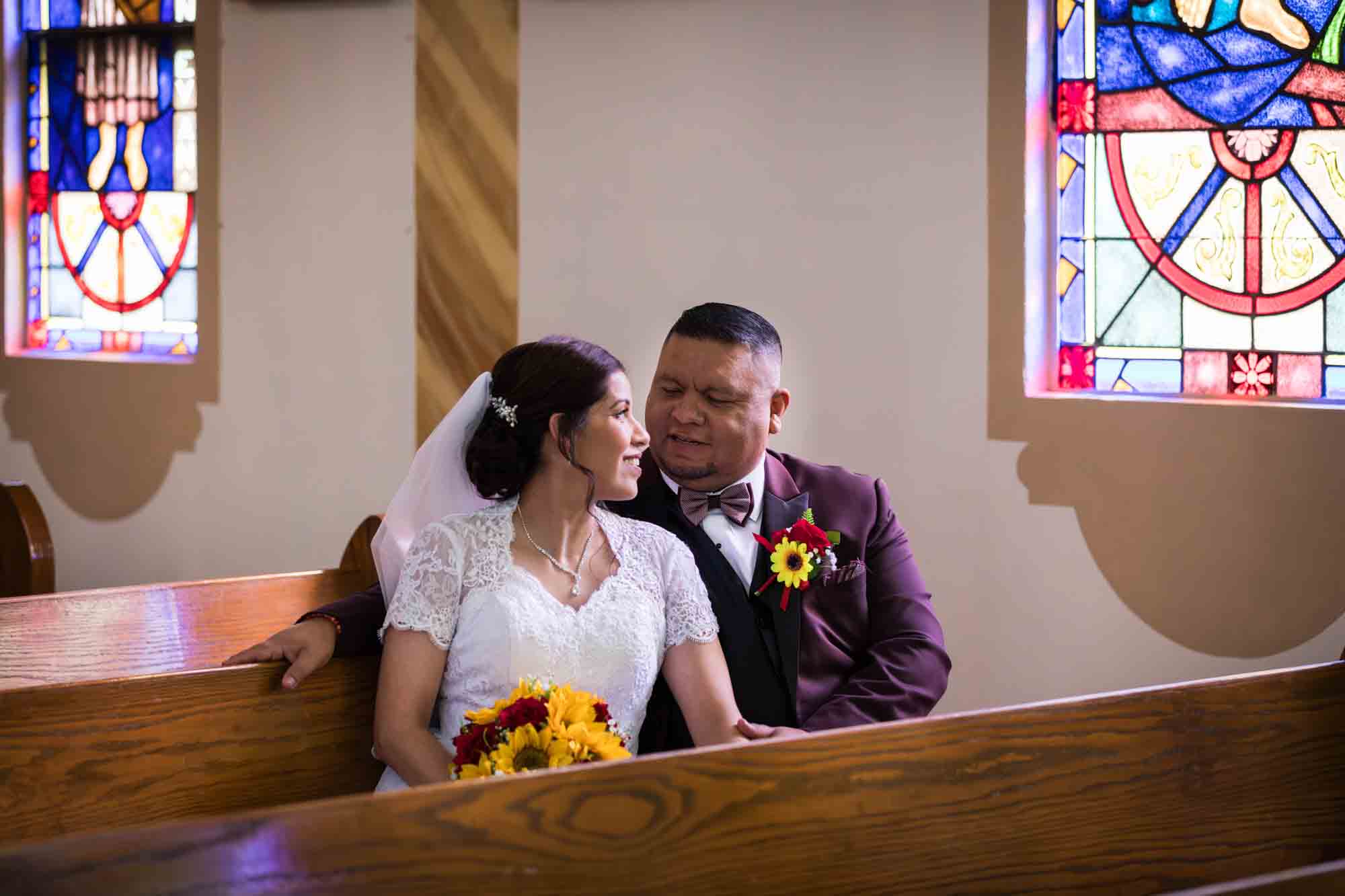 St. Henry Catholic Church wedding photos of bride and groom sitting in pew in front of stained glass window