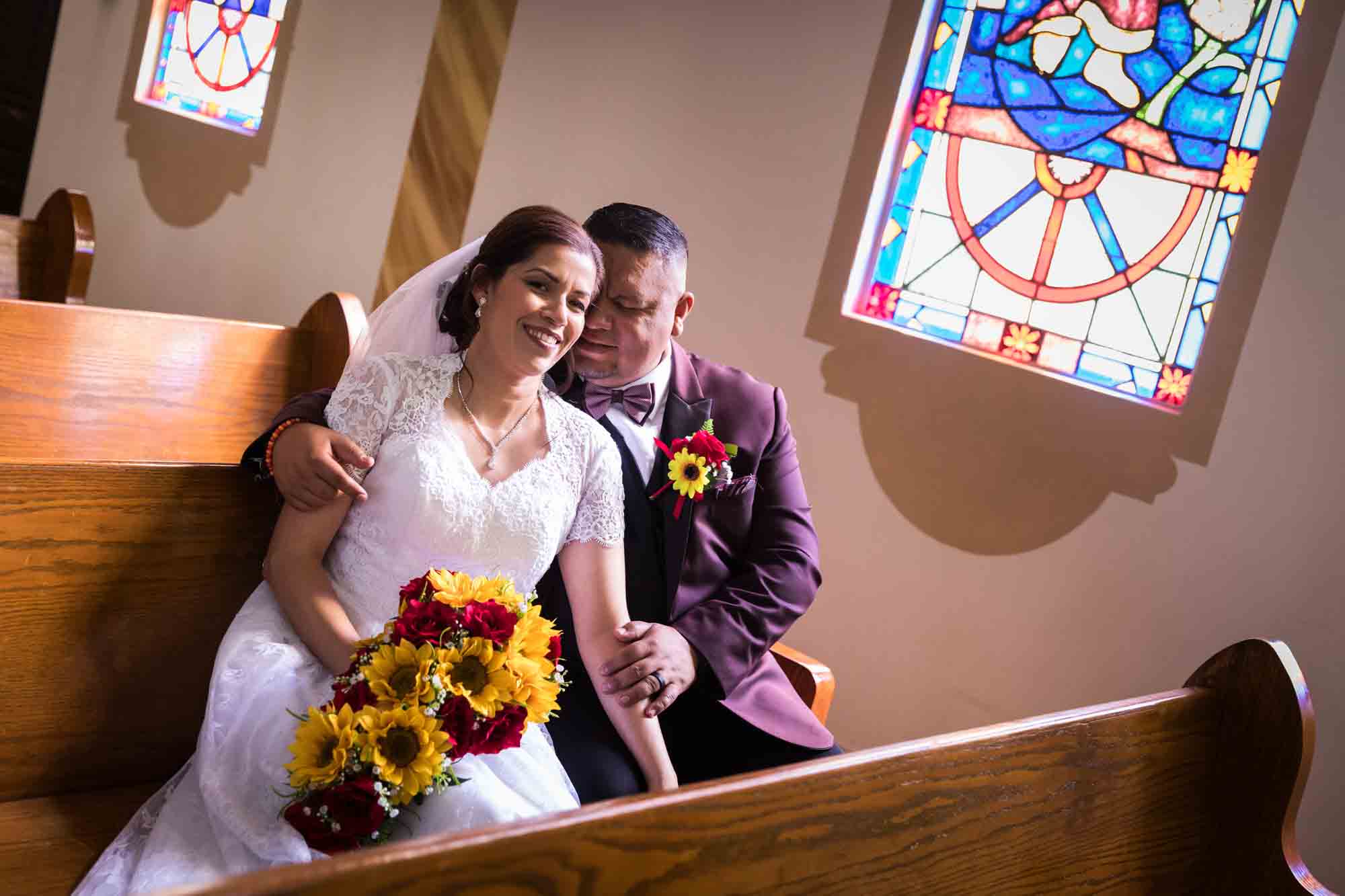 St. Henry Catholic Church wedding photos of bride and groom sitting in pew in front of stained glass window