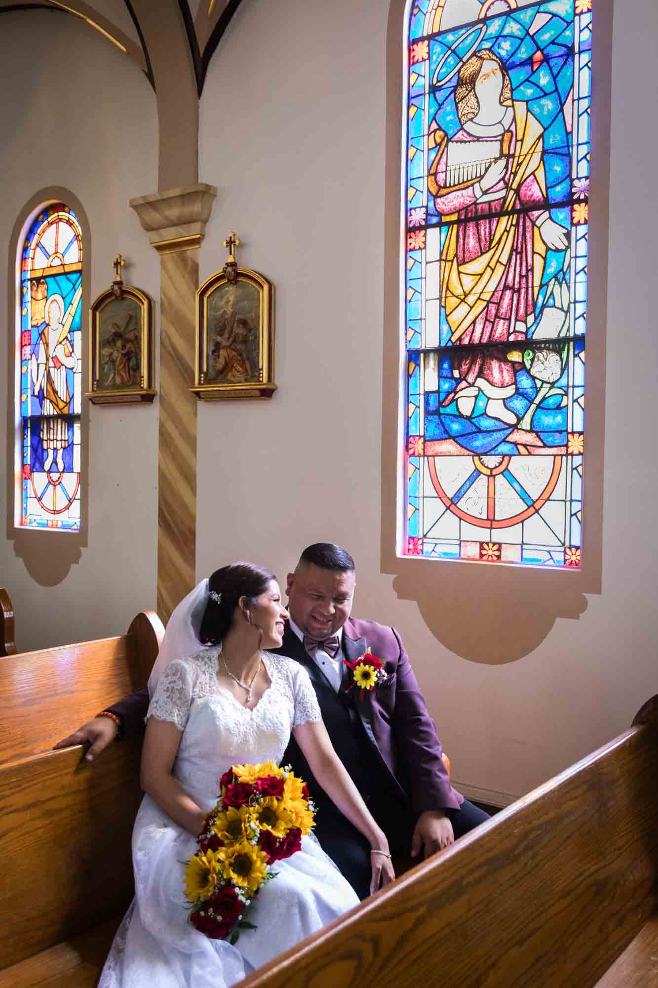 St. Henry Catholic Church wedding photos of bride and groom sitting in pew in front of stained glass window