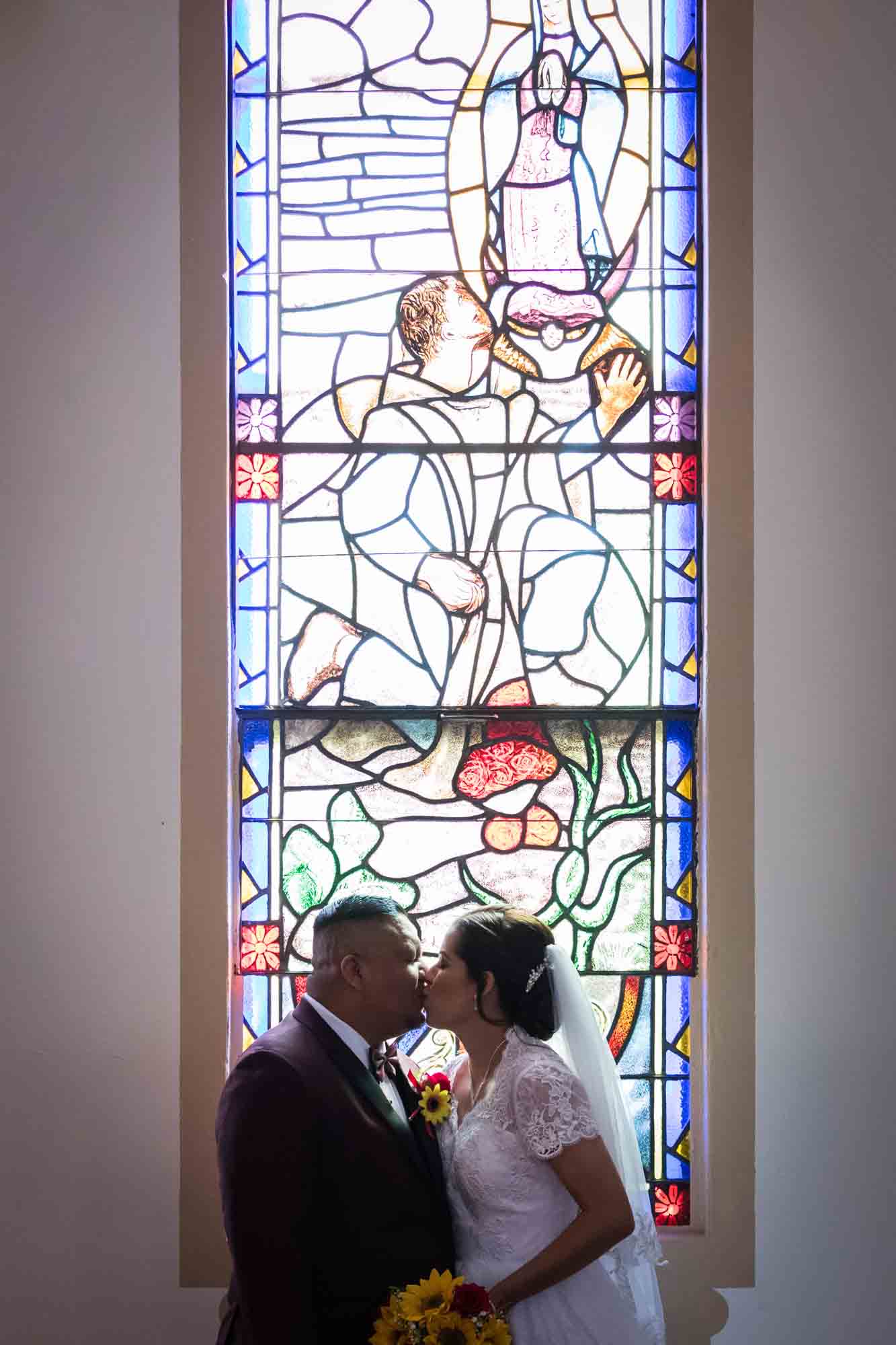 St. Henry Catholic Church wedding photos of bride kissing groom in front of stained glass windows