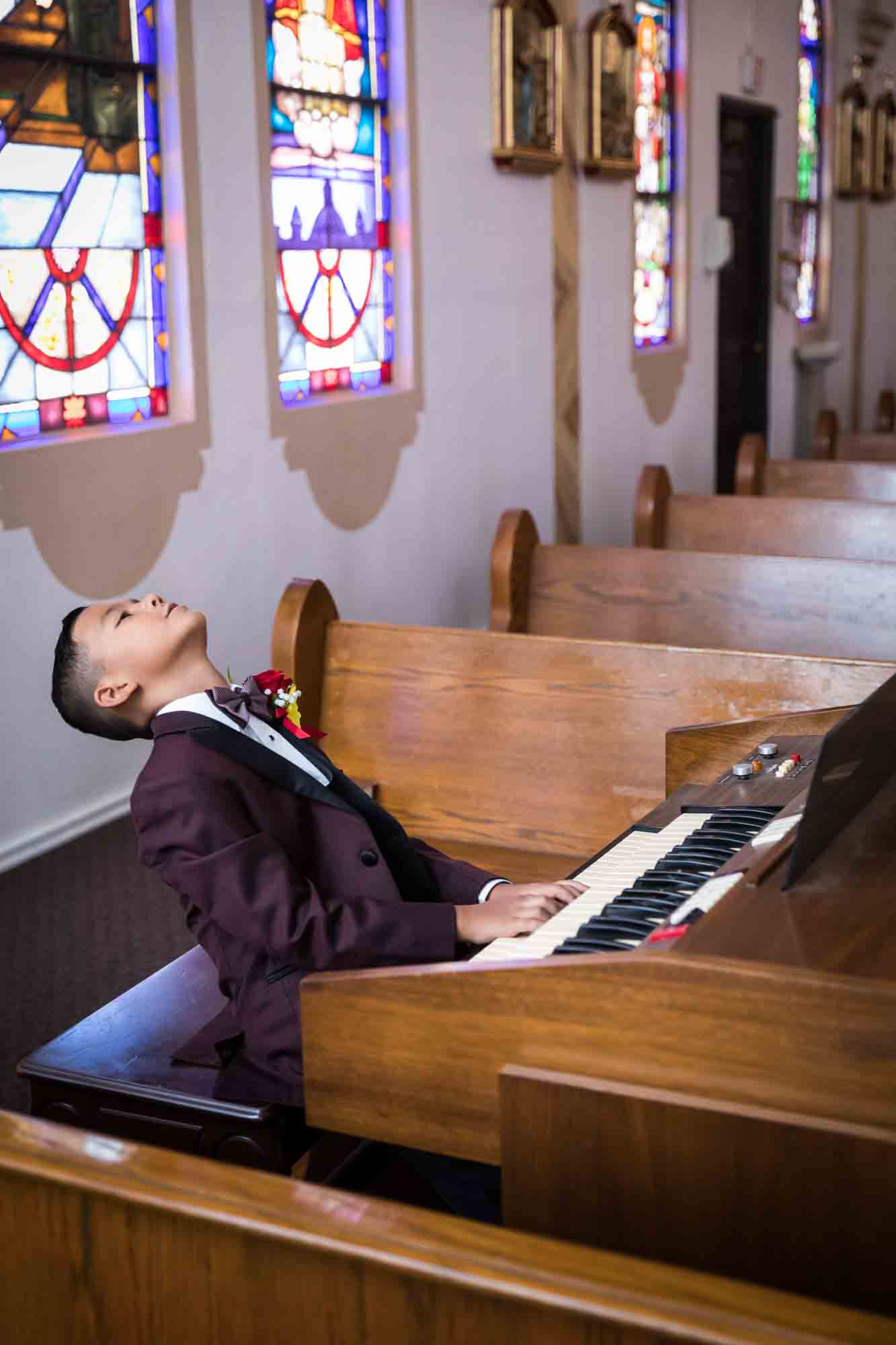 Young boy playing on organ with stained glass windows in background during St. Henry Catholic Church wedding