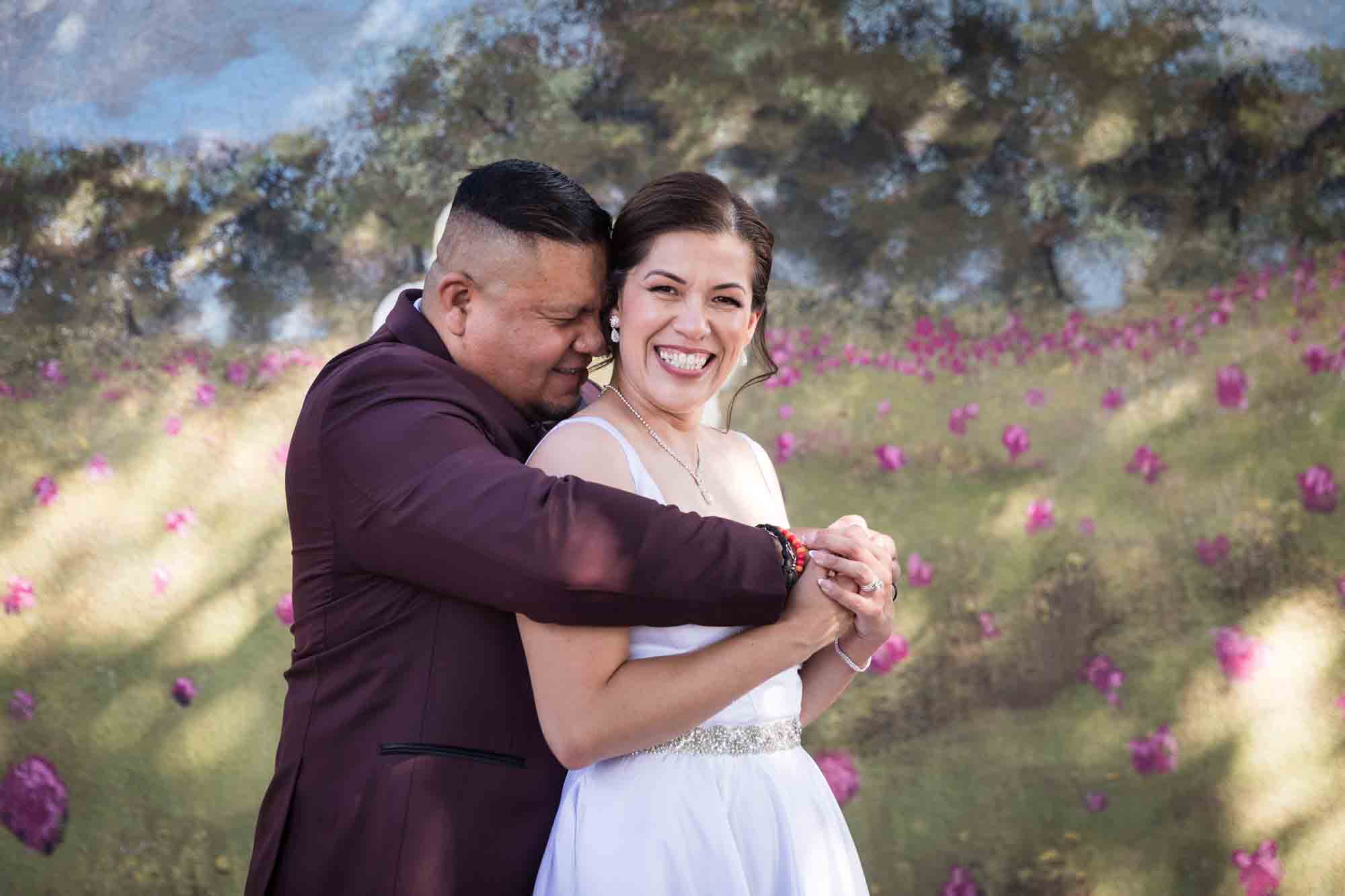 St. Henry Catholic Church wedding photos of groom hugging bride from behind in front of floral mural