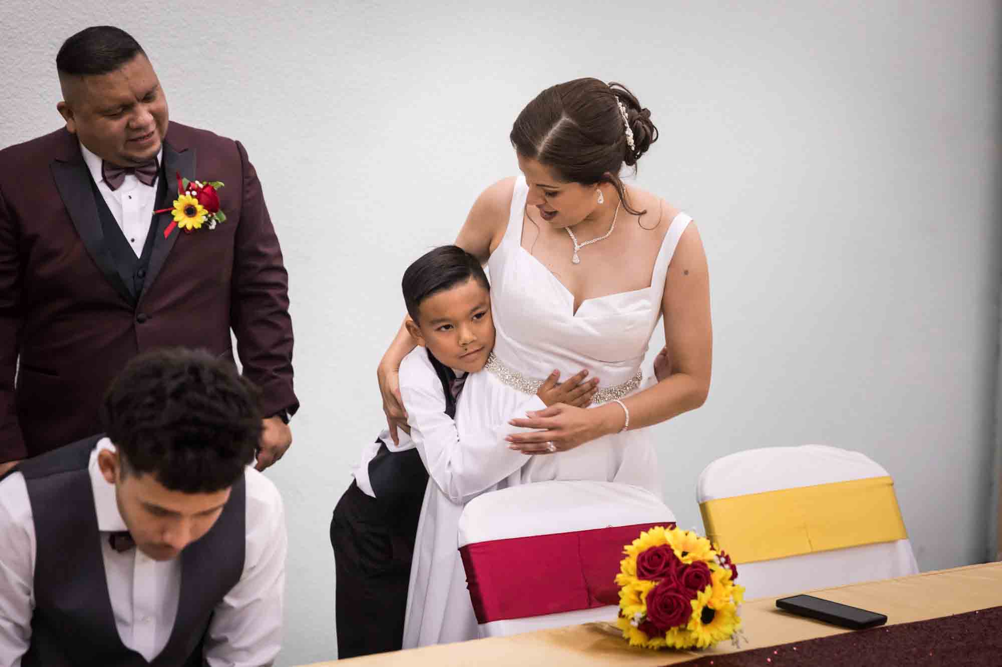 Bride hugging young boy in front of chairs and table during a St. Henry Catholic Church wedding reception