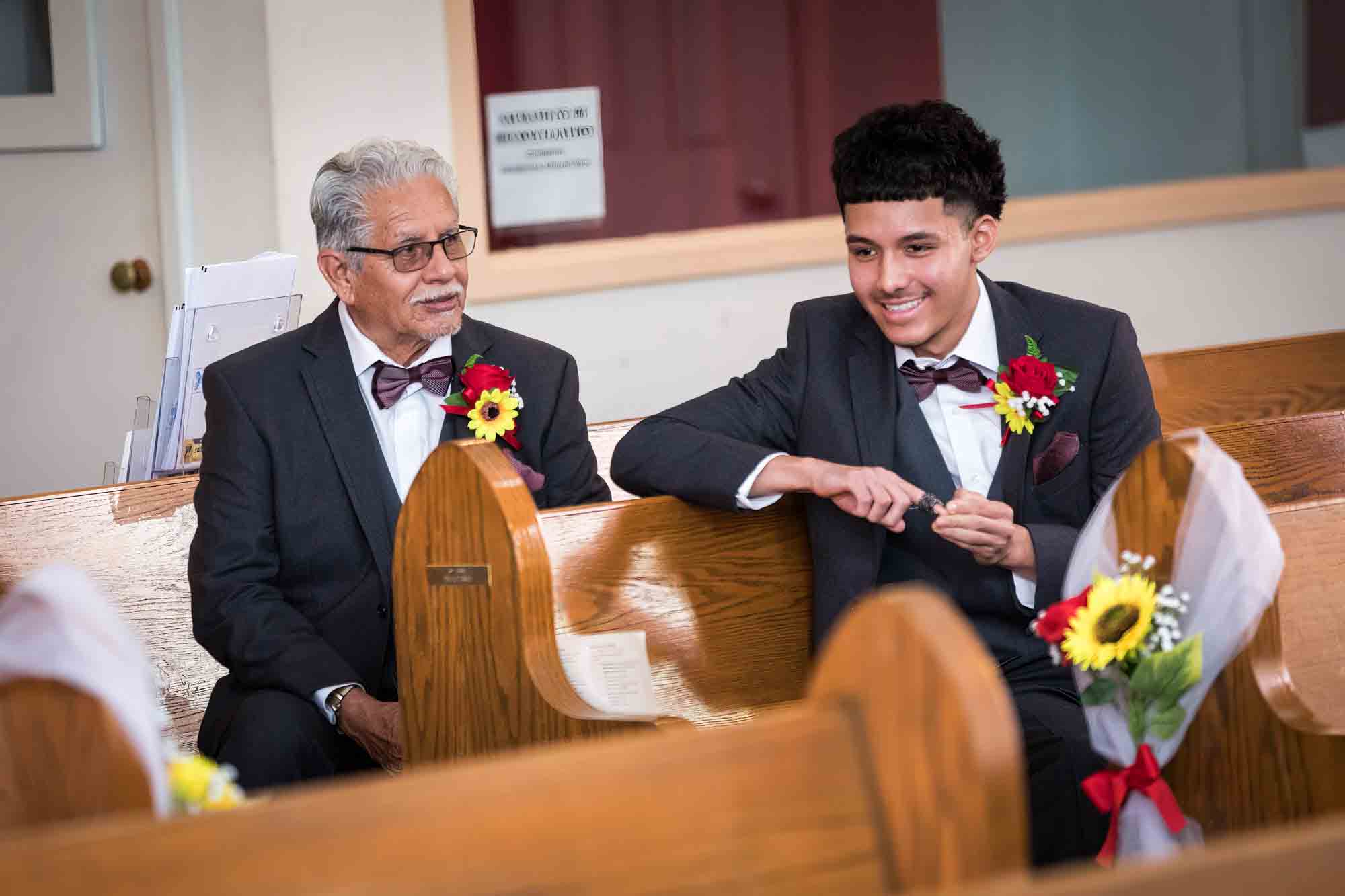 Grandfather and grandson sitting in pew smiling during St. Henry Catholic Church wedding