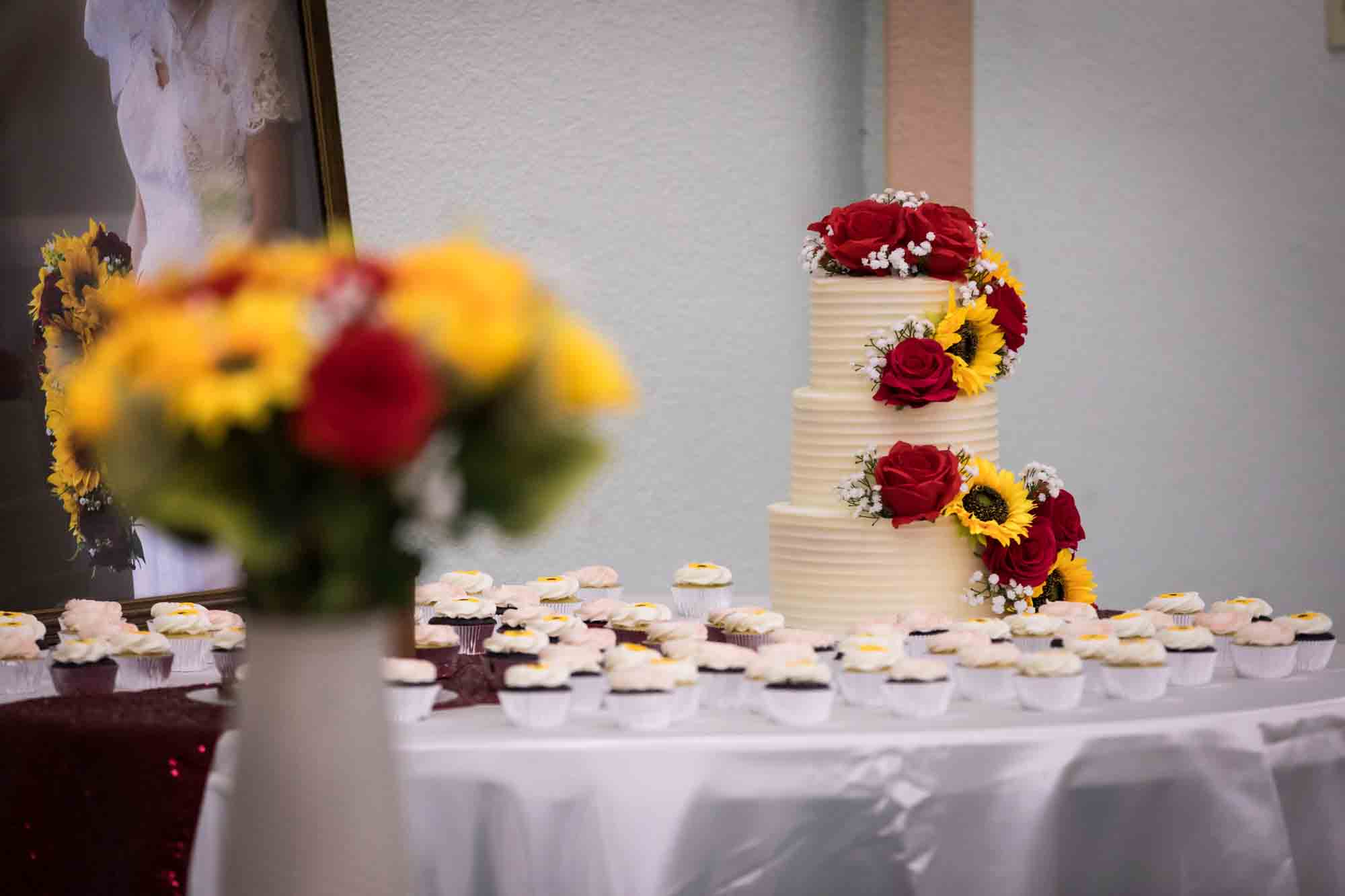 St. Henry Catholic Church wedding photos of wedding cake decorated with sunflowers and red roses with cupcakes in front