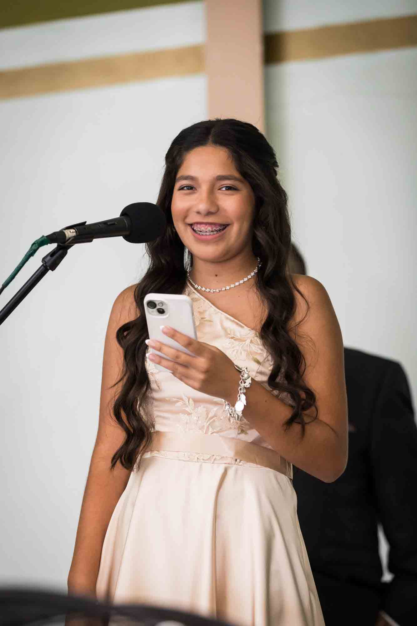 Young girl wearing off shoulder pale beige dress and holding phone during a St. Henry Catholic Church wedding reception