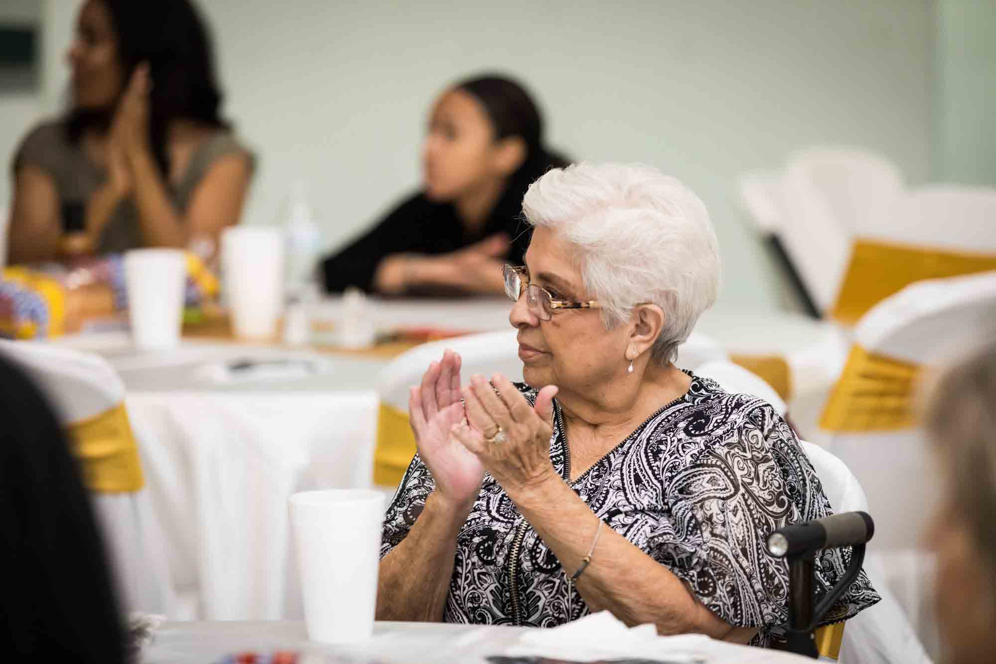 Woman with short white hair and glasses clapping during a St. Henry Catholic Church wedding reception