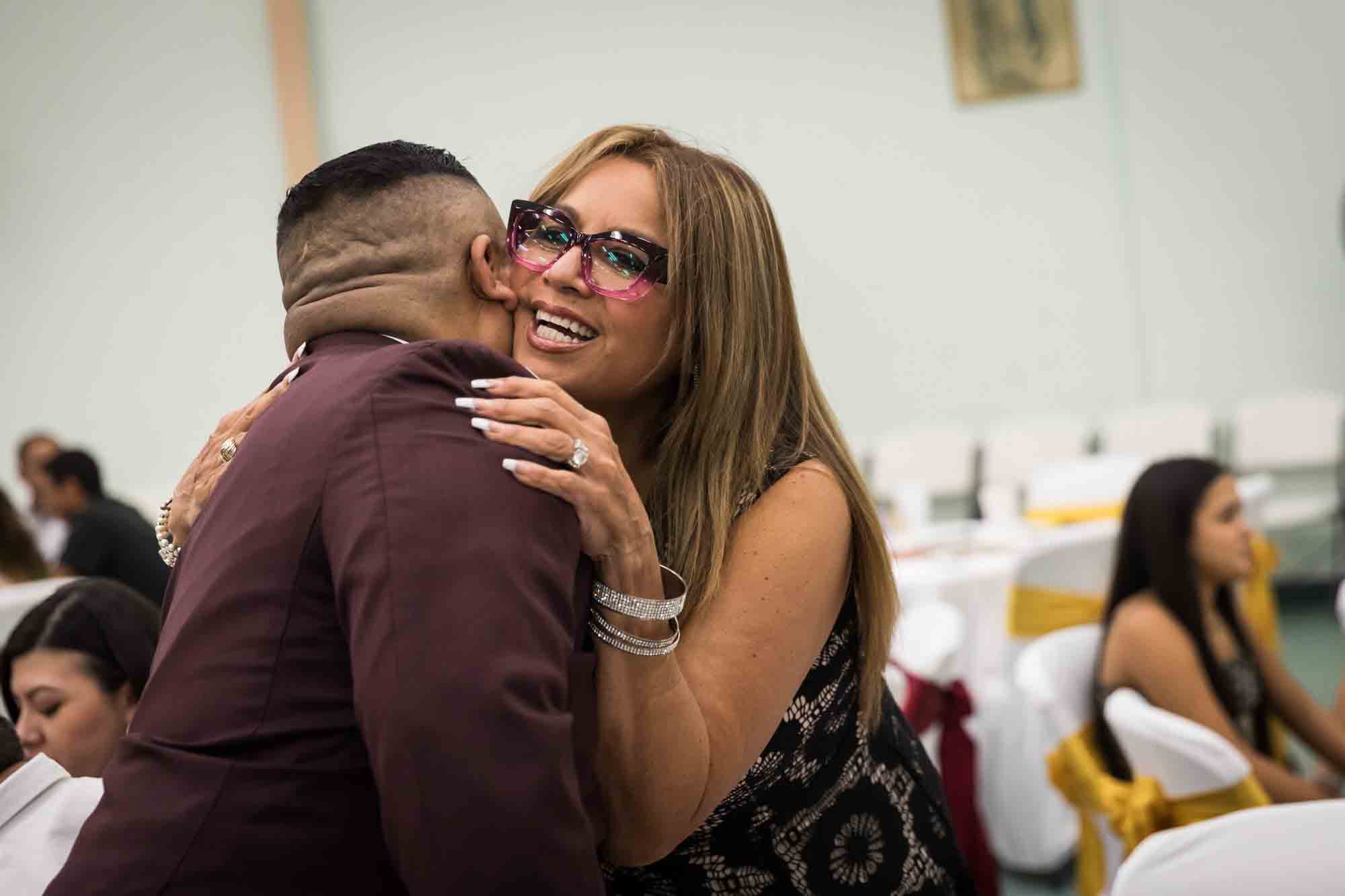 Groom hugging woman wearing pink and black glasses during a St. Henry Catholic Church wedding reception