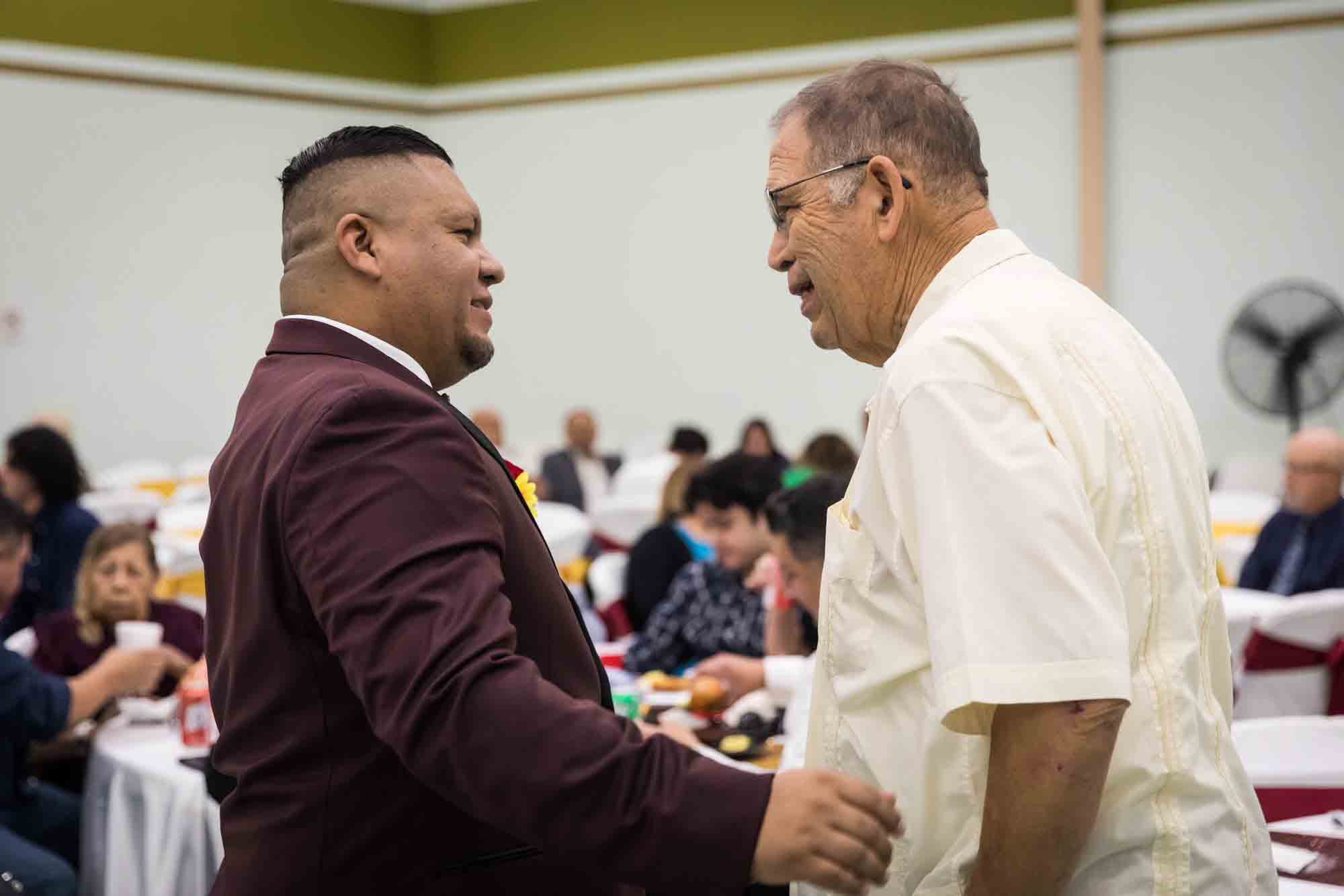 Groom talking to older man wearing off white shirt during a St. Henry Catholic Church wedding reception