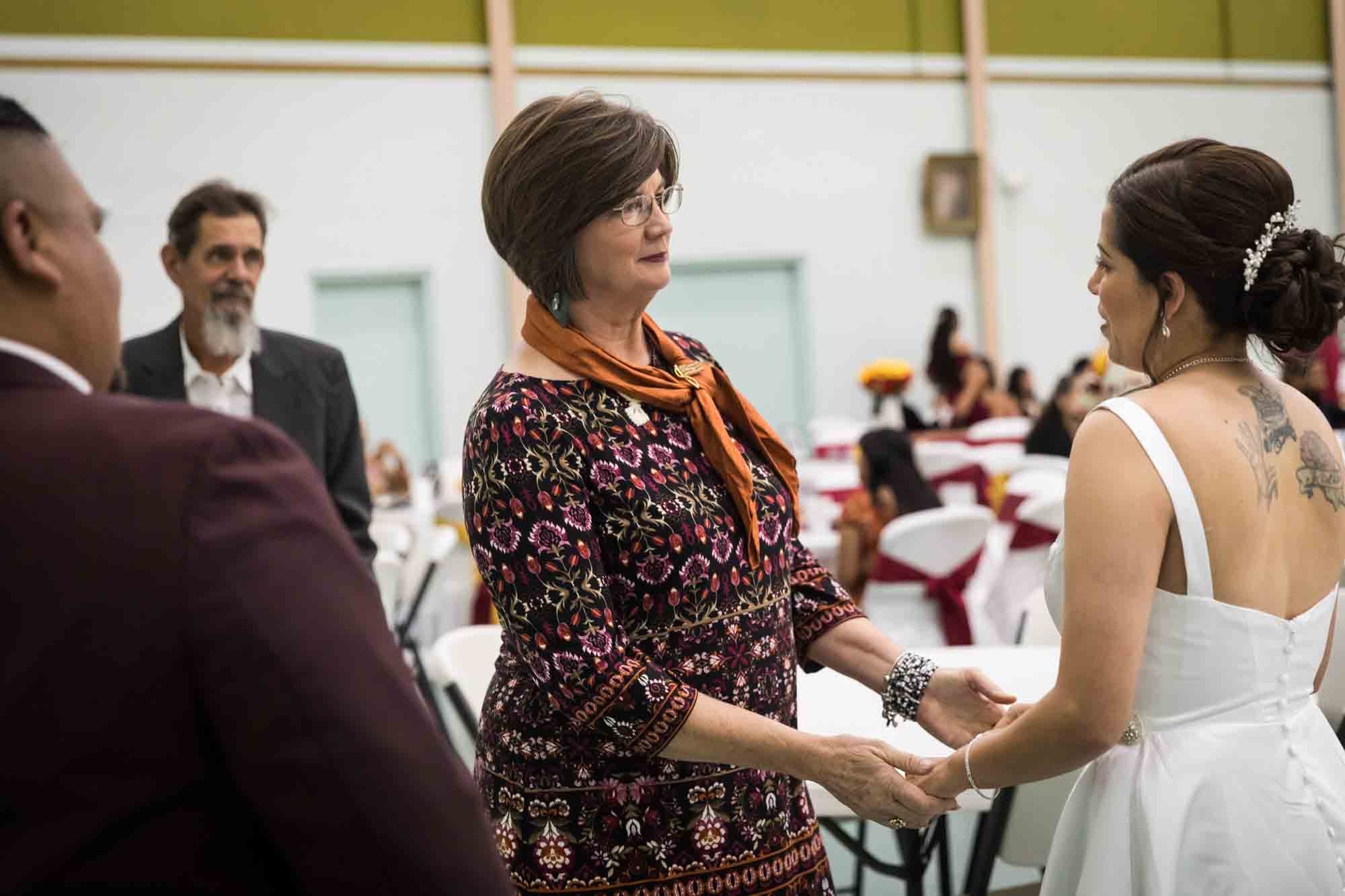 Bride holding hands with woman with short brown hair and orange scarf during a St. Henry Catholic Church wedding reception