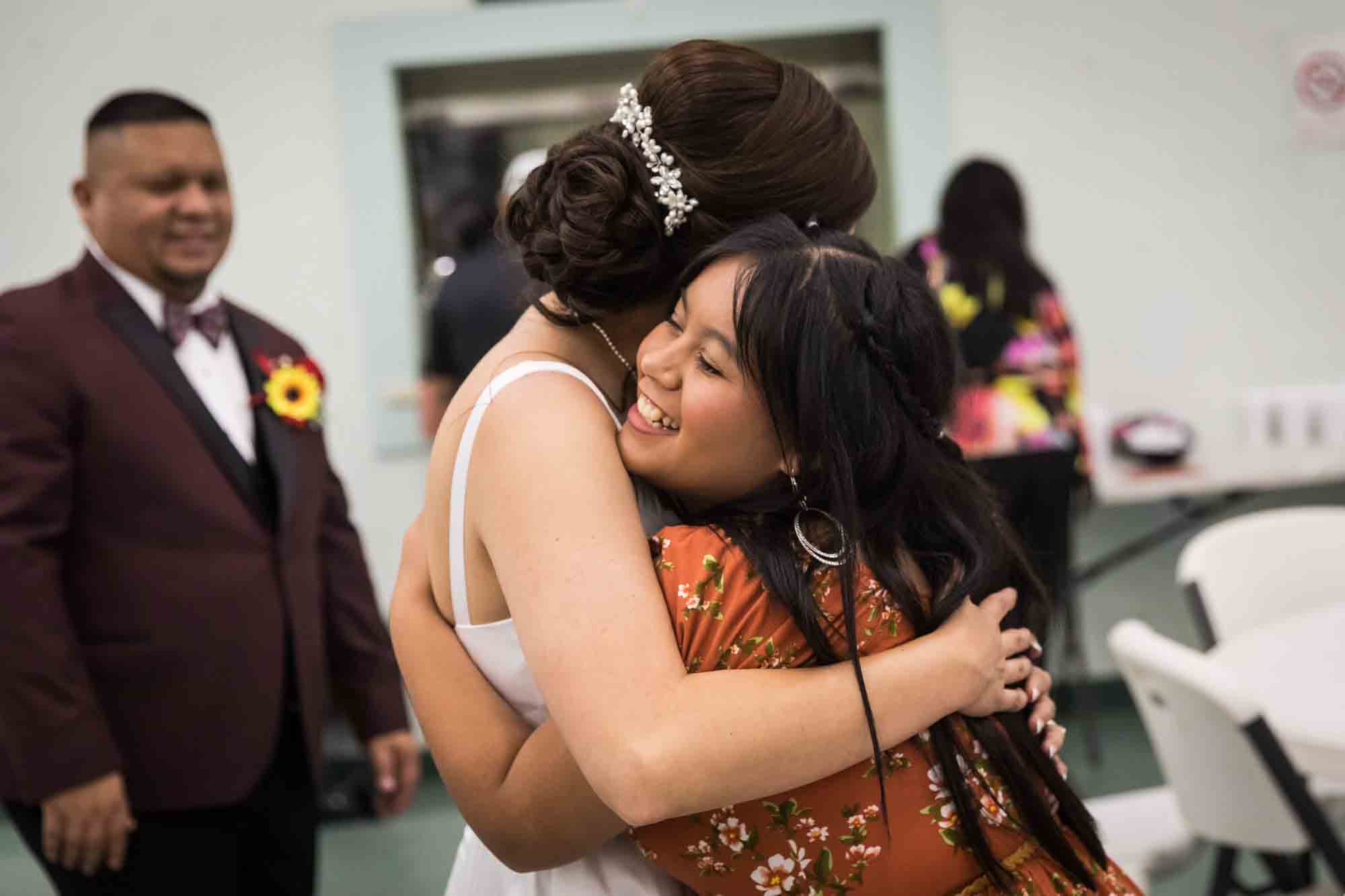 Bride hugging girl with long hair and orange, floral dress during a St. Henry Catholic Church wedding reception