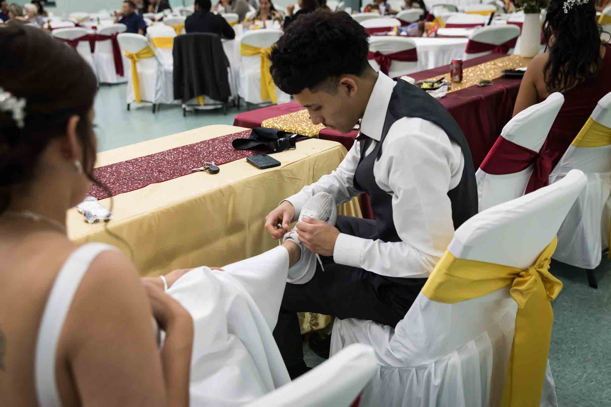 Young man tying white tennis shoe of bride at table during a St. Henry Catholic Church wedding reception