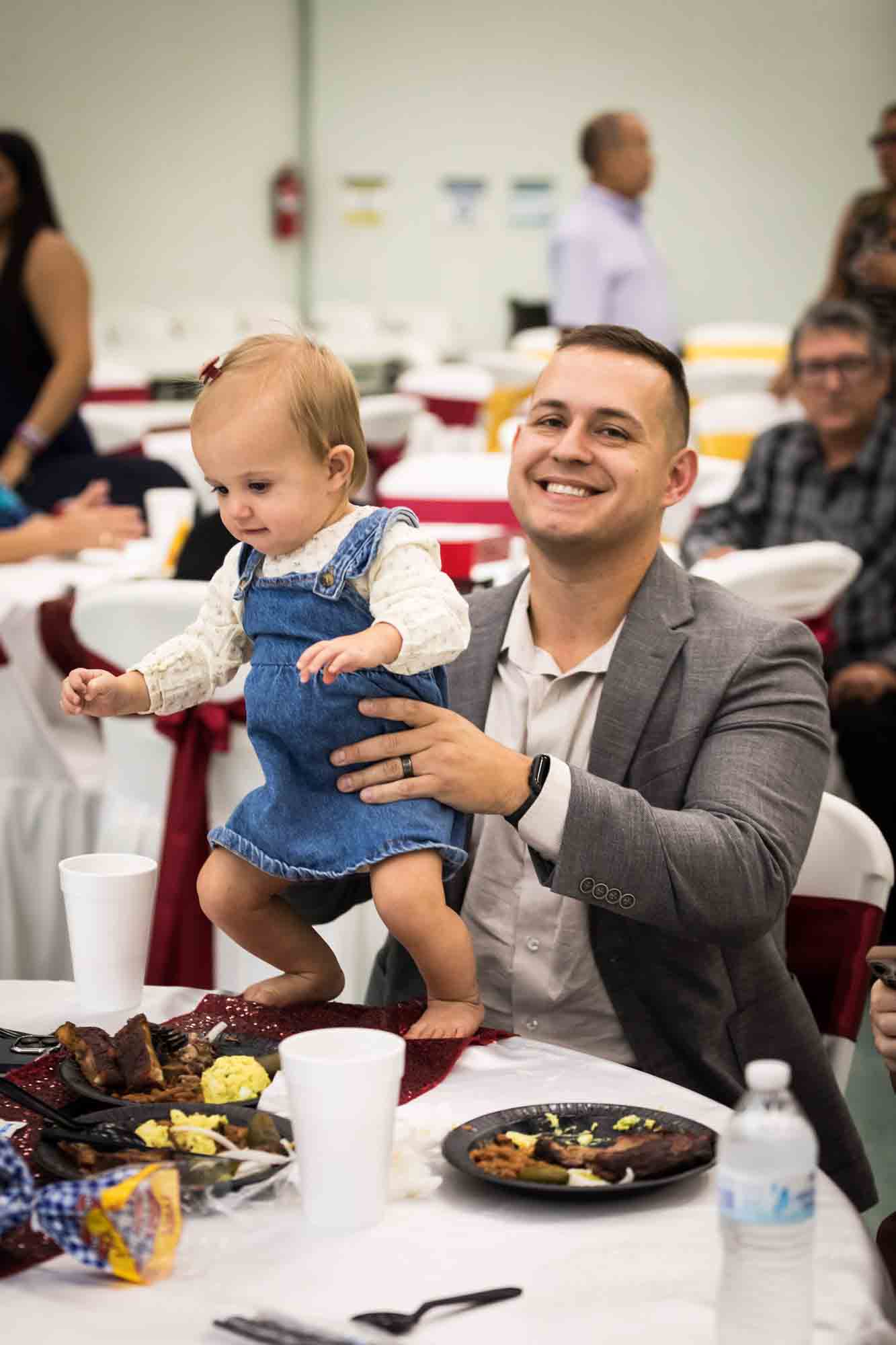 Father holding toddler on a table during a St. Henry Catholic Church wedding reception