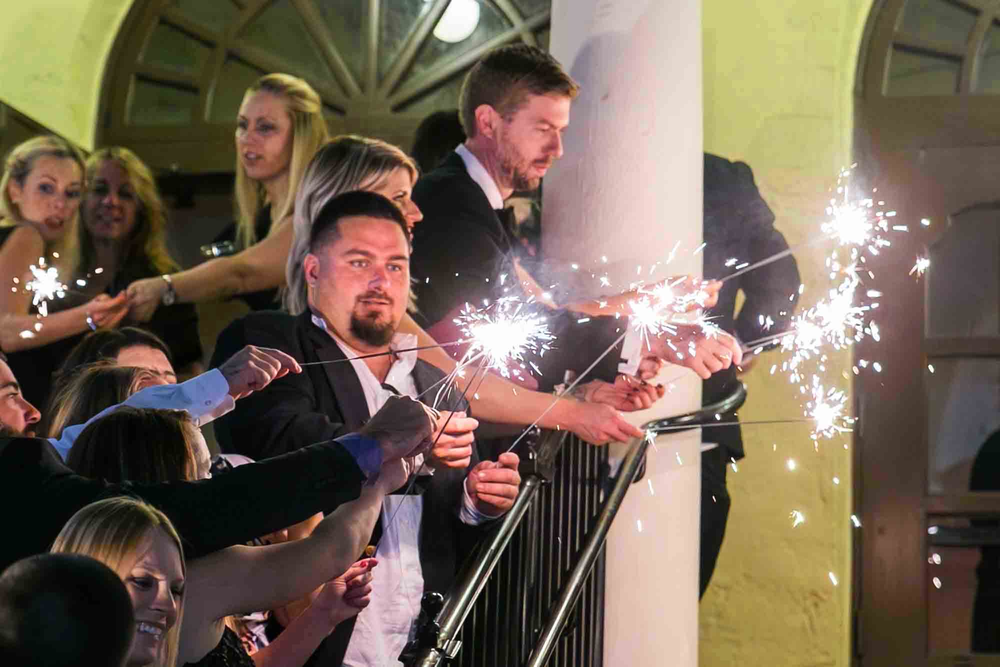 Wedding guests enjoying sparklers outside on a staircase for an article on how to have fireworks at an event in San Antonio