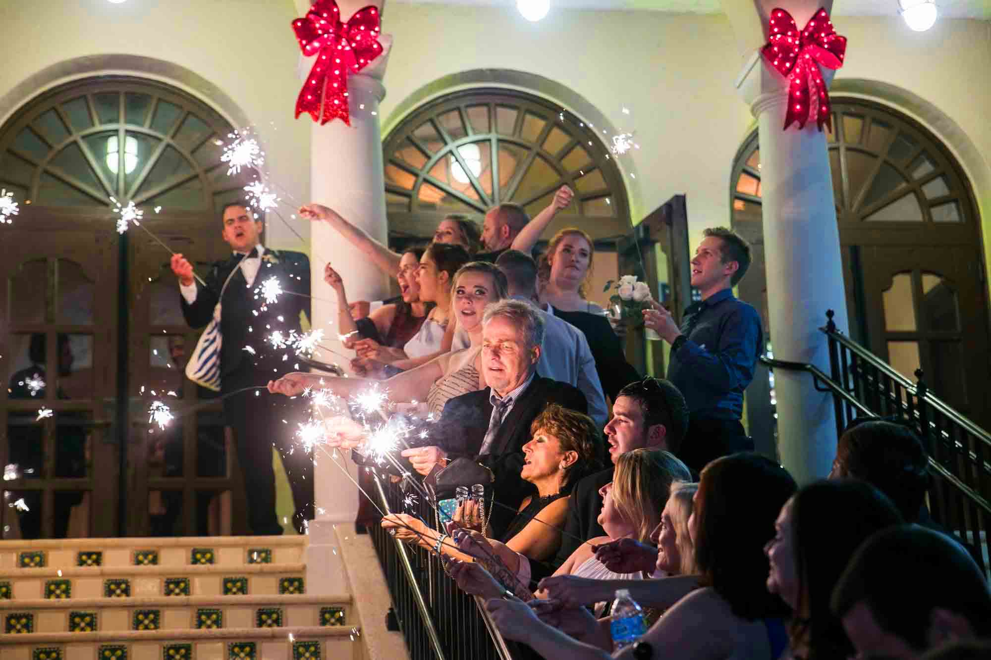 Wedding guests enjoying sparklers outside on a staircase for an article on how to have fireworks at an event in San Antonio