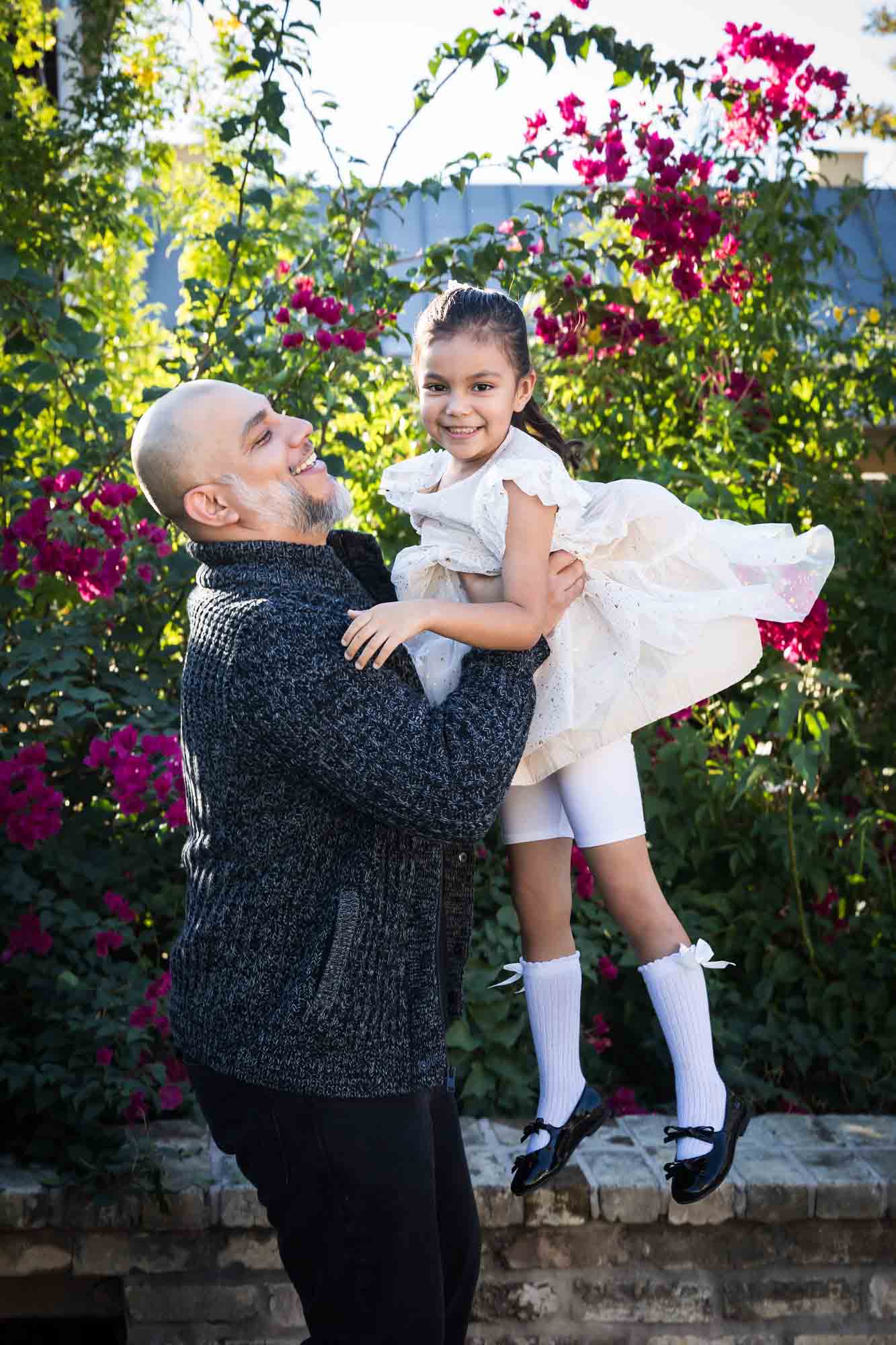 Father throwing little girl in the air in front of bushes during a La Villita family portrait session