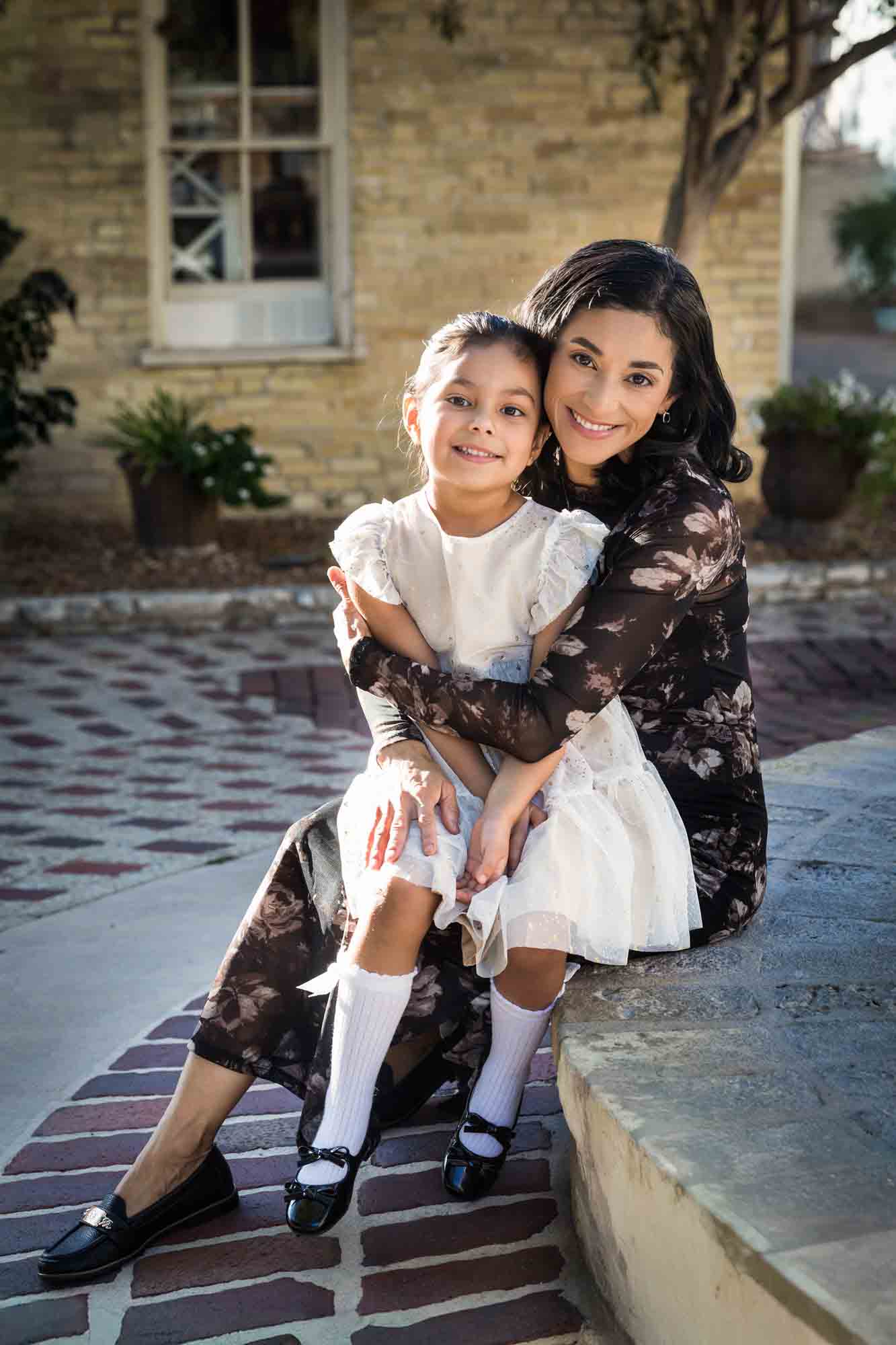 Mother and daughter hugging while sitting on side of fountain during a La Villita family portrait session