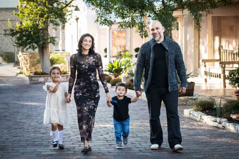 Parents holding hands and walking with little boy and girl on cobblestone street during a La Villita family portrait session