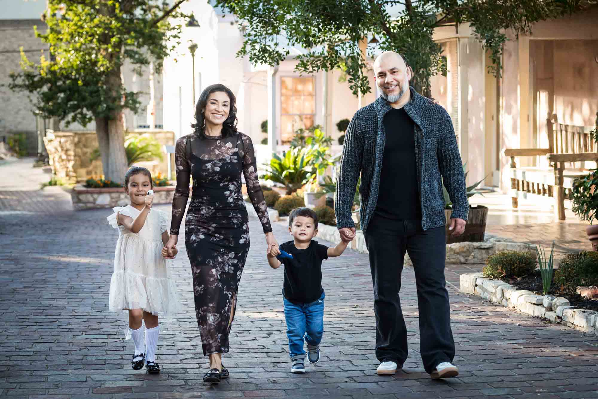 Parents holding hands and walking with little boy and girl on cobblestone street during a La Villita family portrait session