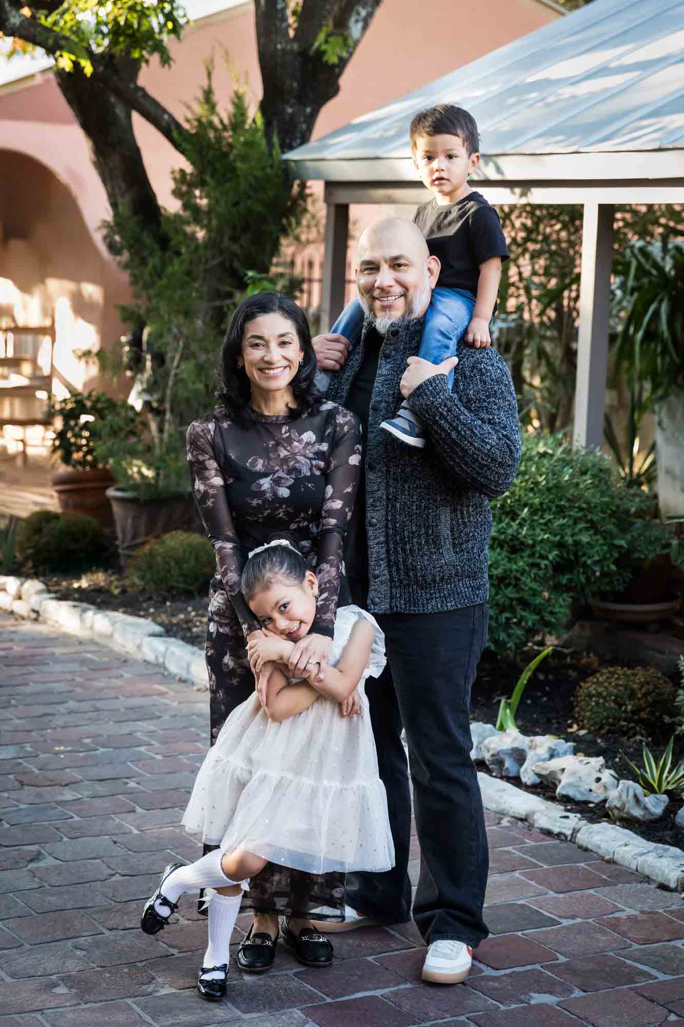 Father with little boy on his shoulder standing with mother and little girl on cobblestone street during a La Villita family portrait session