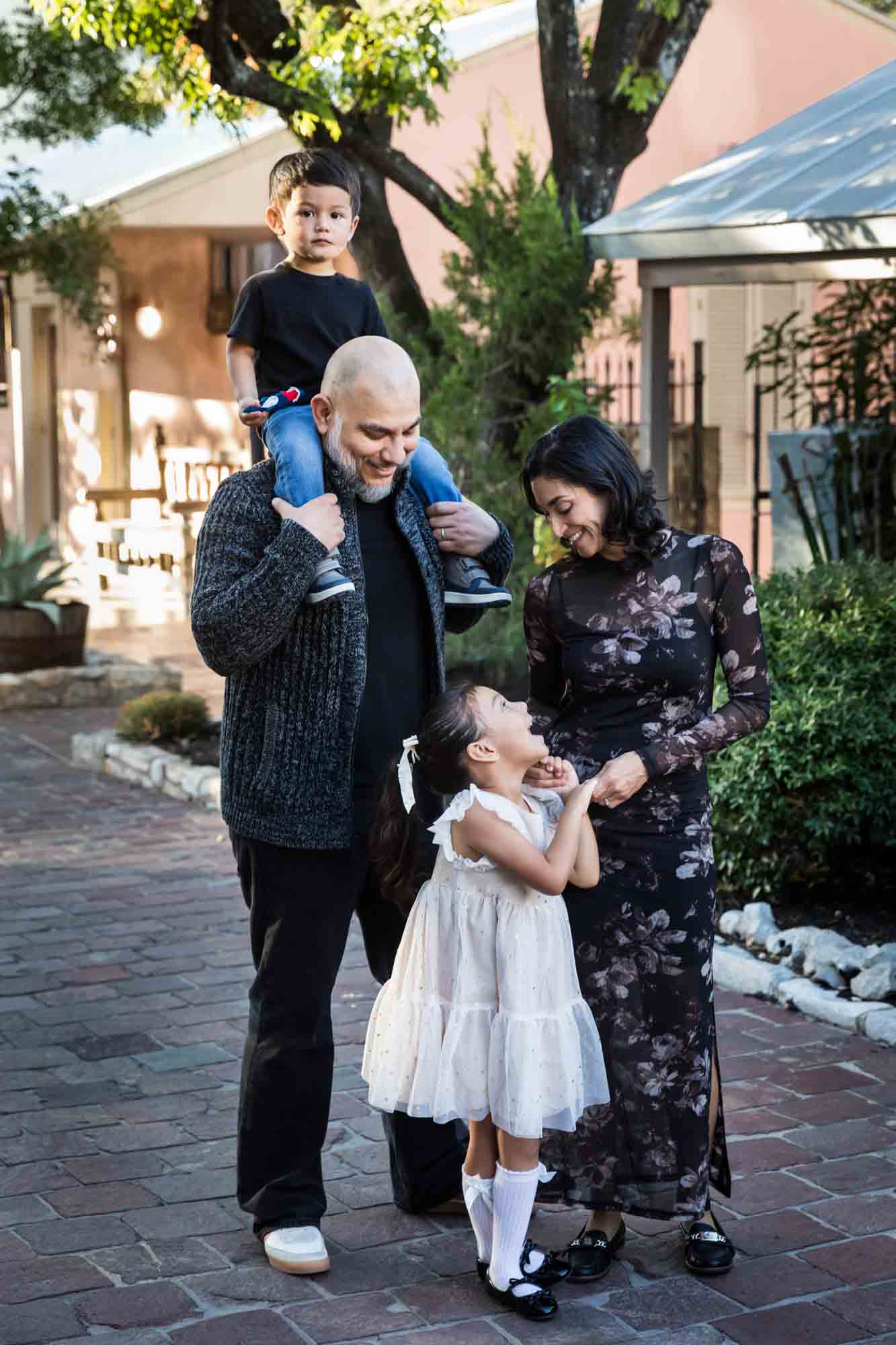 Father with little boy on his shoulder standing with mother and little girl on cobblestone street during a La Villita family portrait session