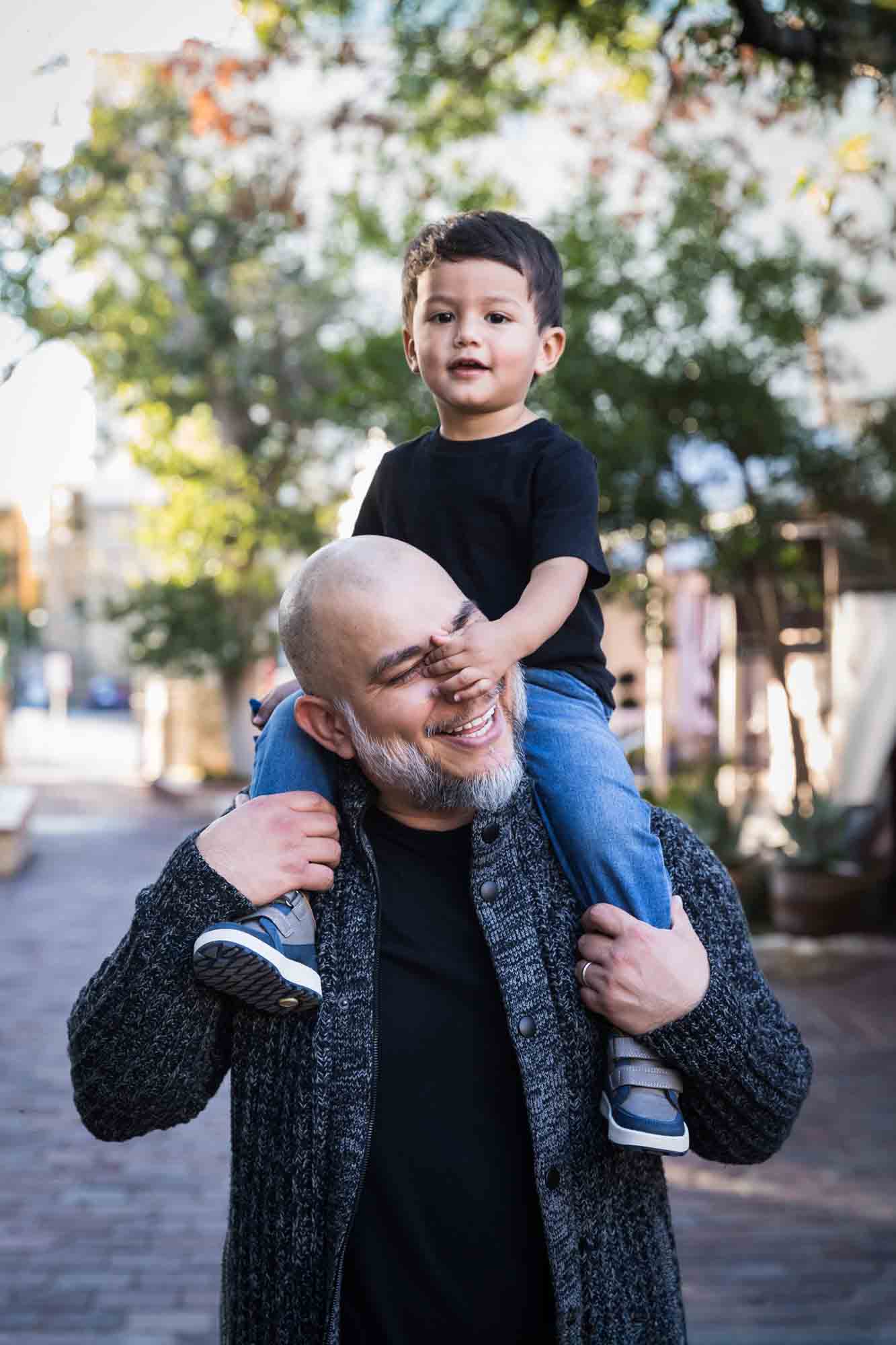 Father holding little boy on his shoulders and little boy grabbing father's nose