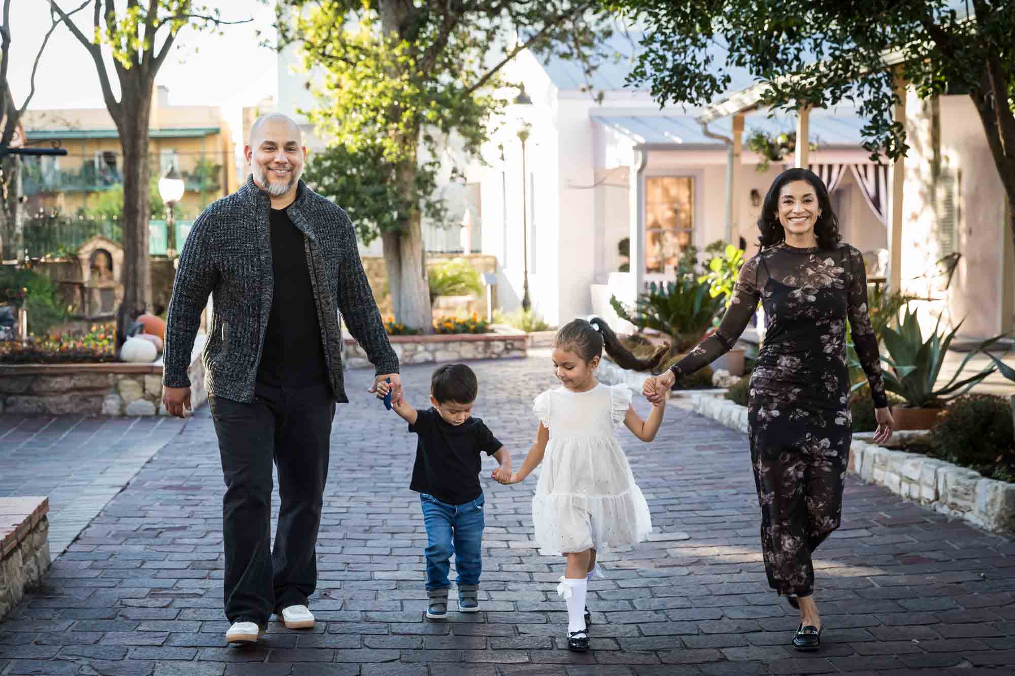 Parents holding hands and walking with little boy and girl on cobblestone street during a La Villita family portrait session