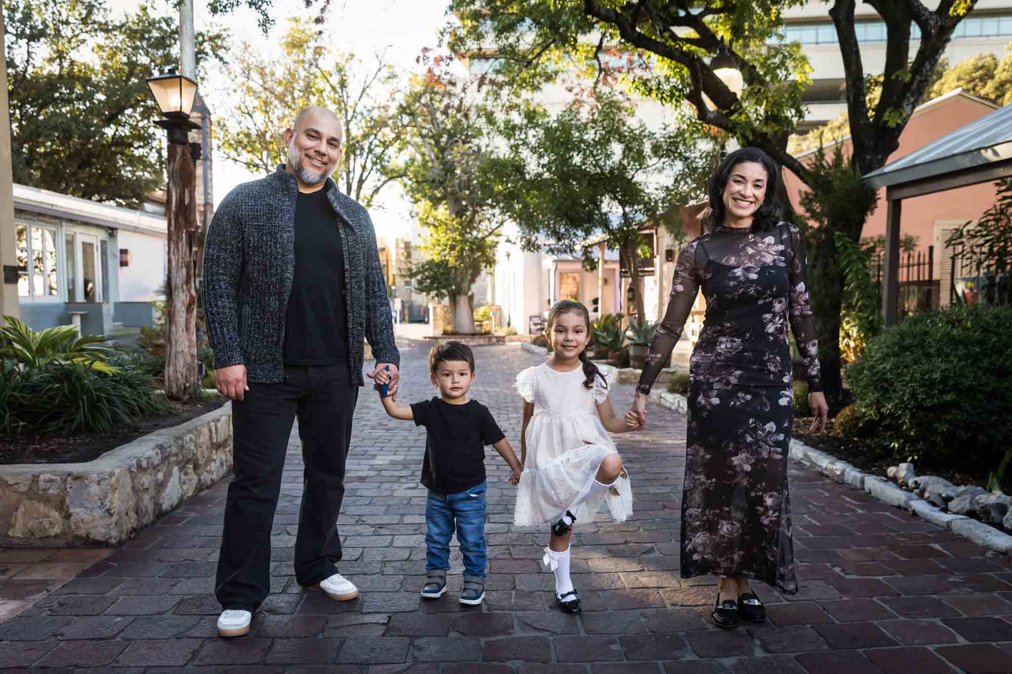 Parents holding hands with little boy and girl on cobblestone street during a La Villita family portrait session