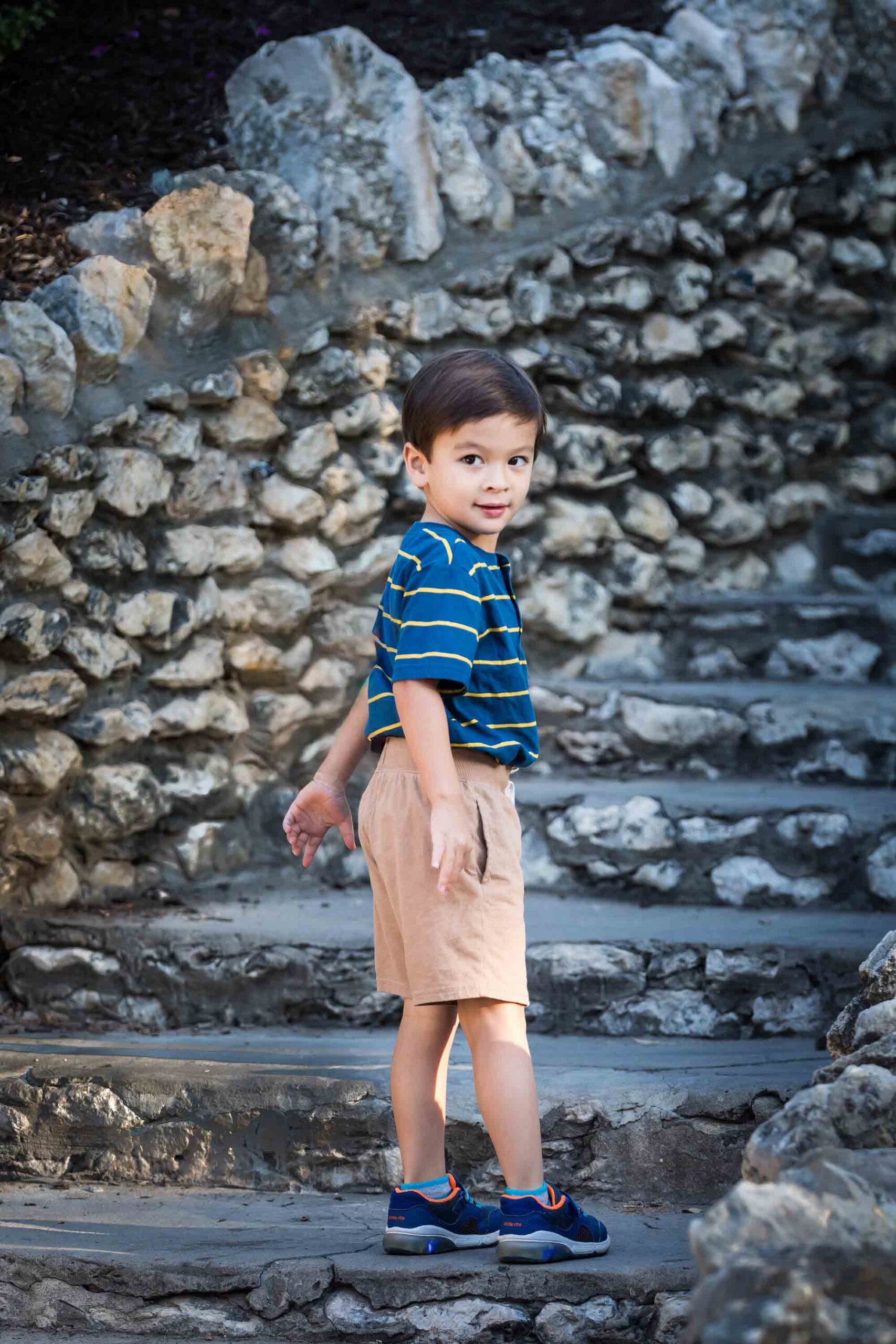 Little boy wearing khaki shorts and striped shirt in front of stone staircase for an article on photo tips for families with young children