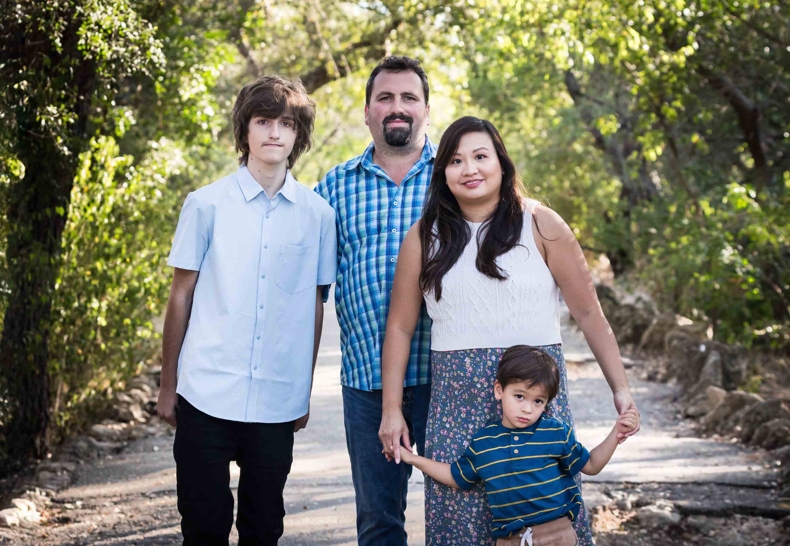 Parents with teenager boy and young boy standing in pathway in forested park for an article on photo tips for families with young children