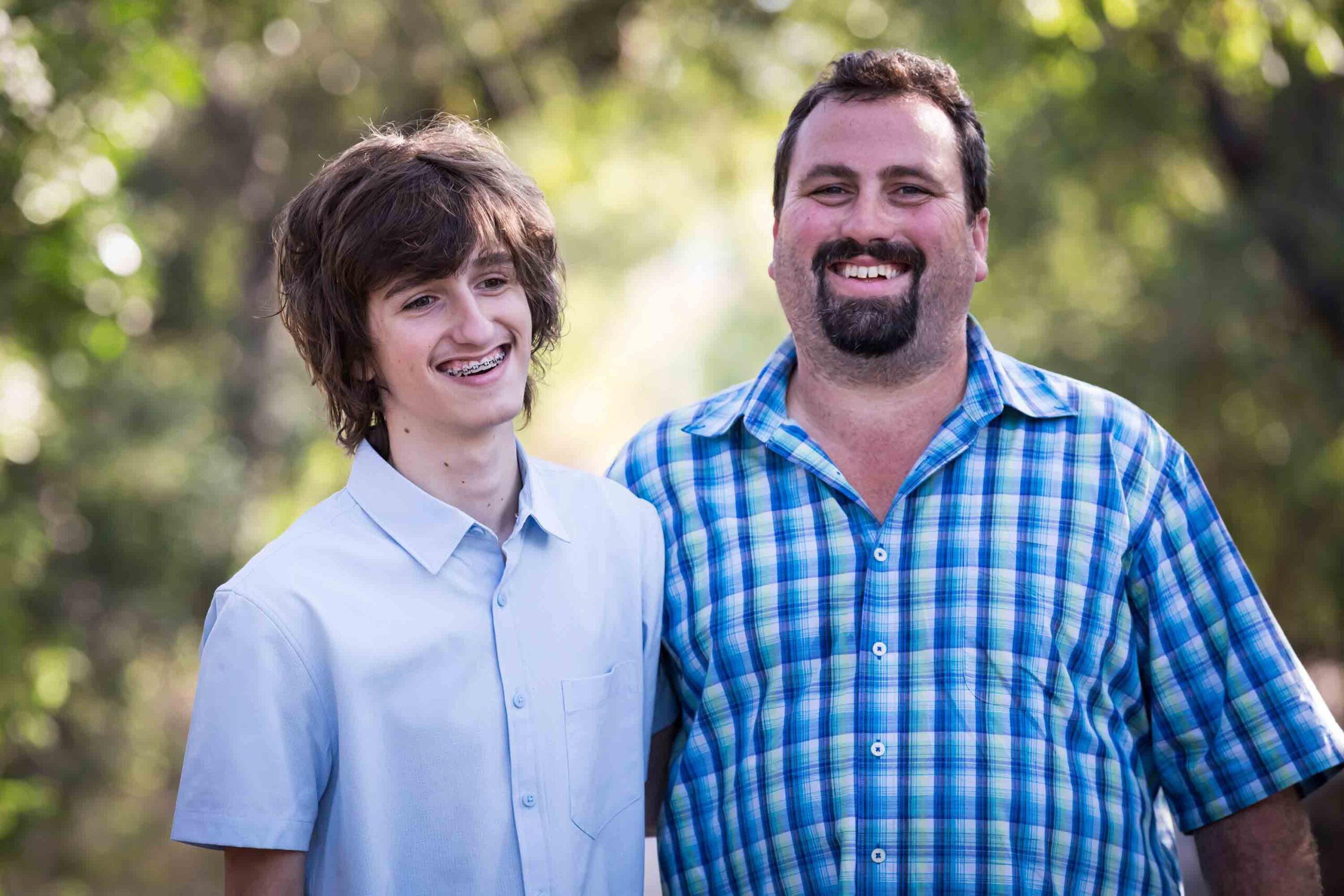 Father and teenage son wearing blue shirts with forest in background