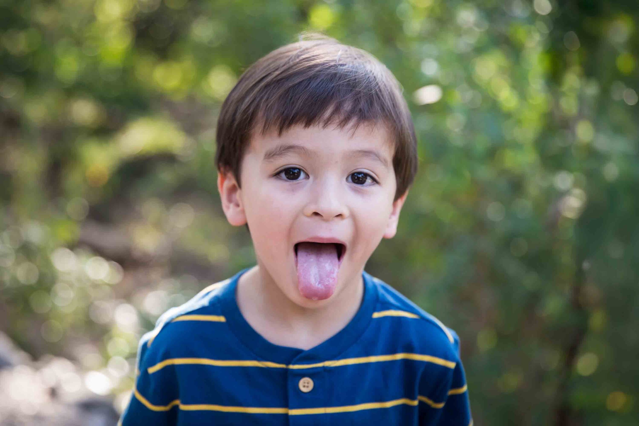 Little boy with brown hair and striped shirt sticking out tongue for an article on photo tips for families with young children