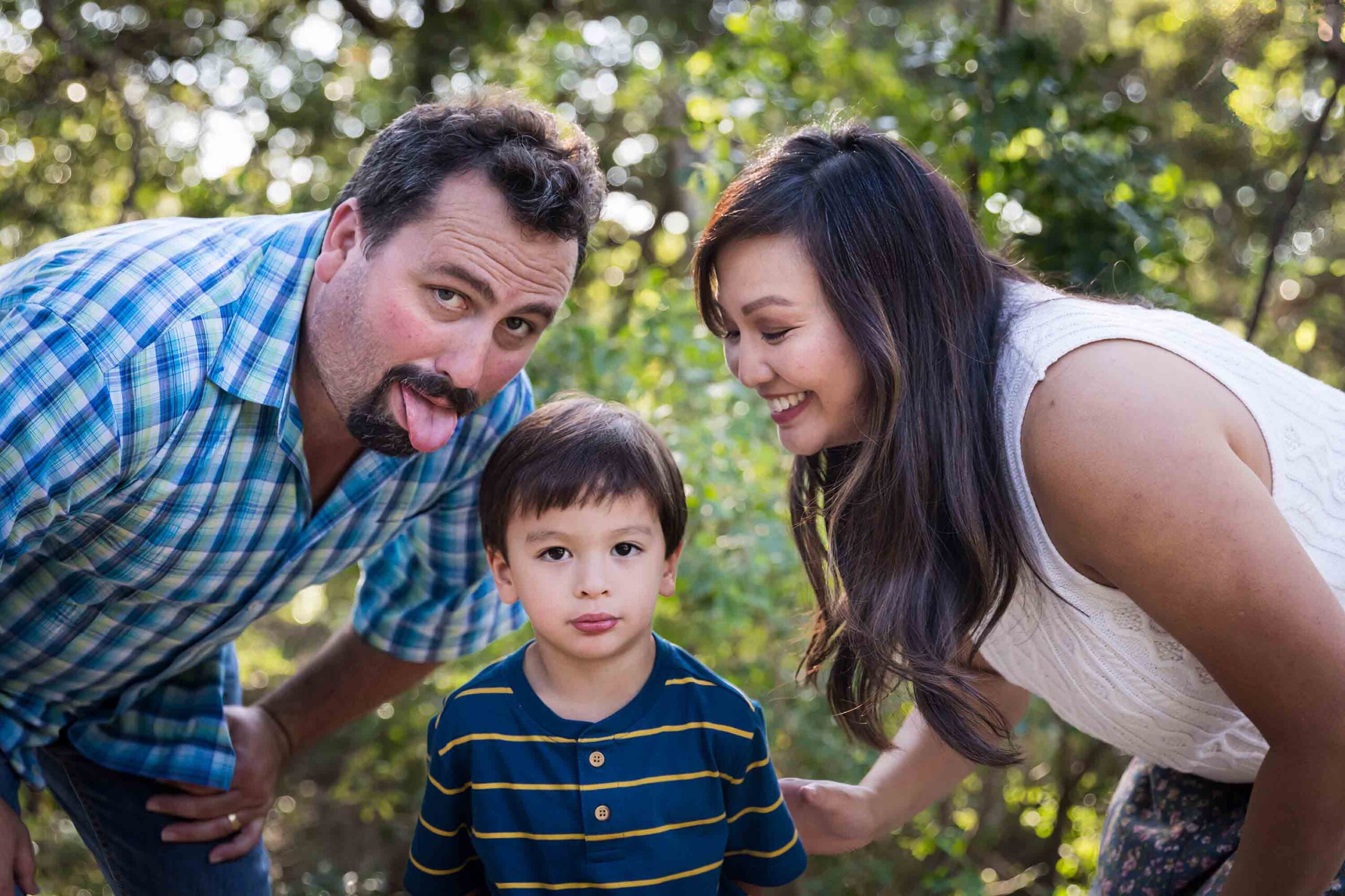 Parents making funny faces with little boy in front of forest