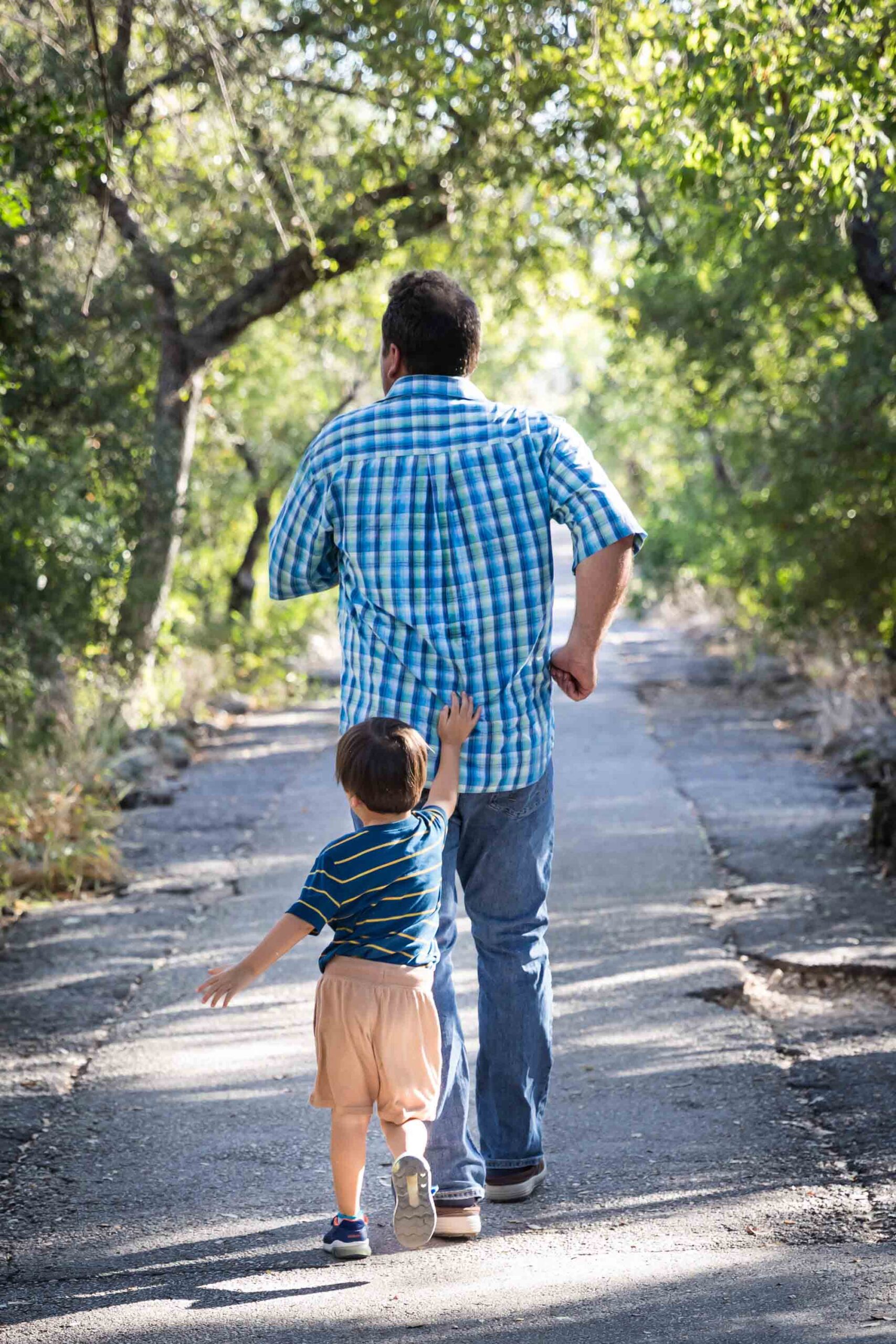 Little boy chasing father down pathway in forested park