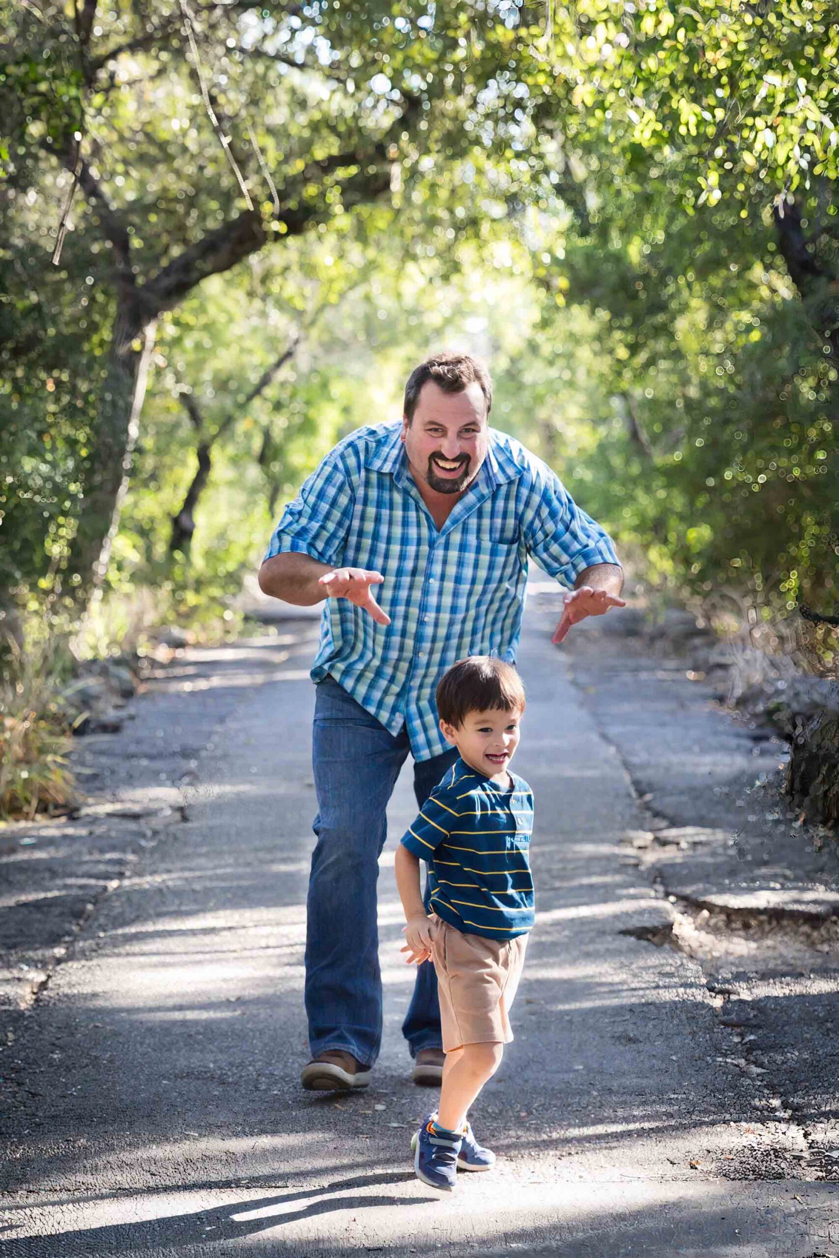 Father chasing little boy down pathway in forested park