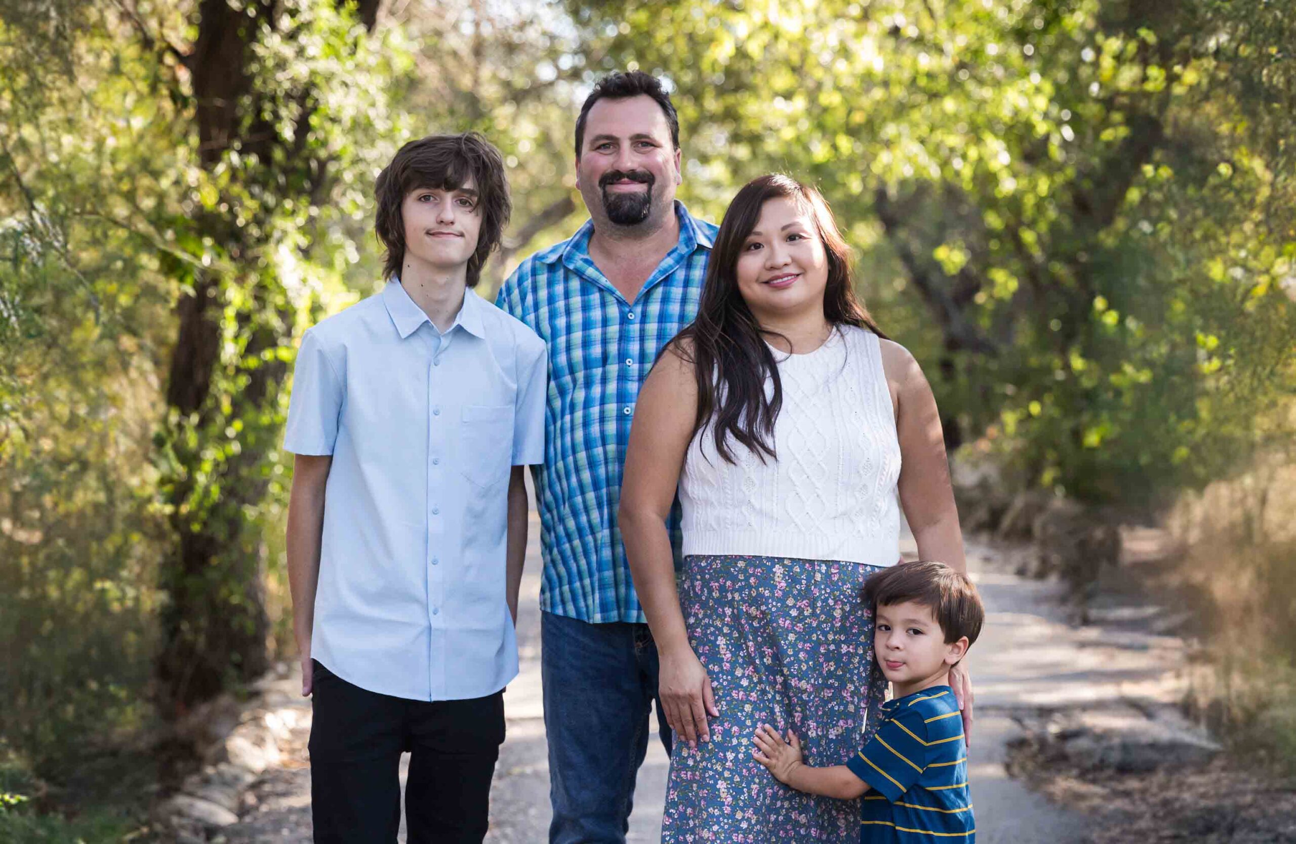 Parents with teenager boy and young boy standing in pathway in forested park for an article on photo tips for families with young children