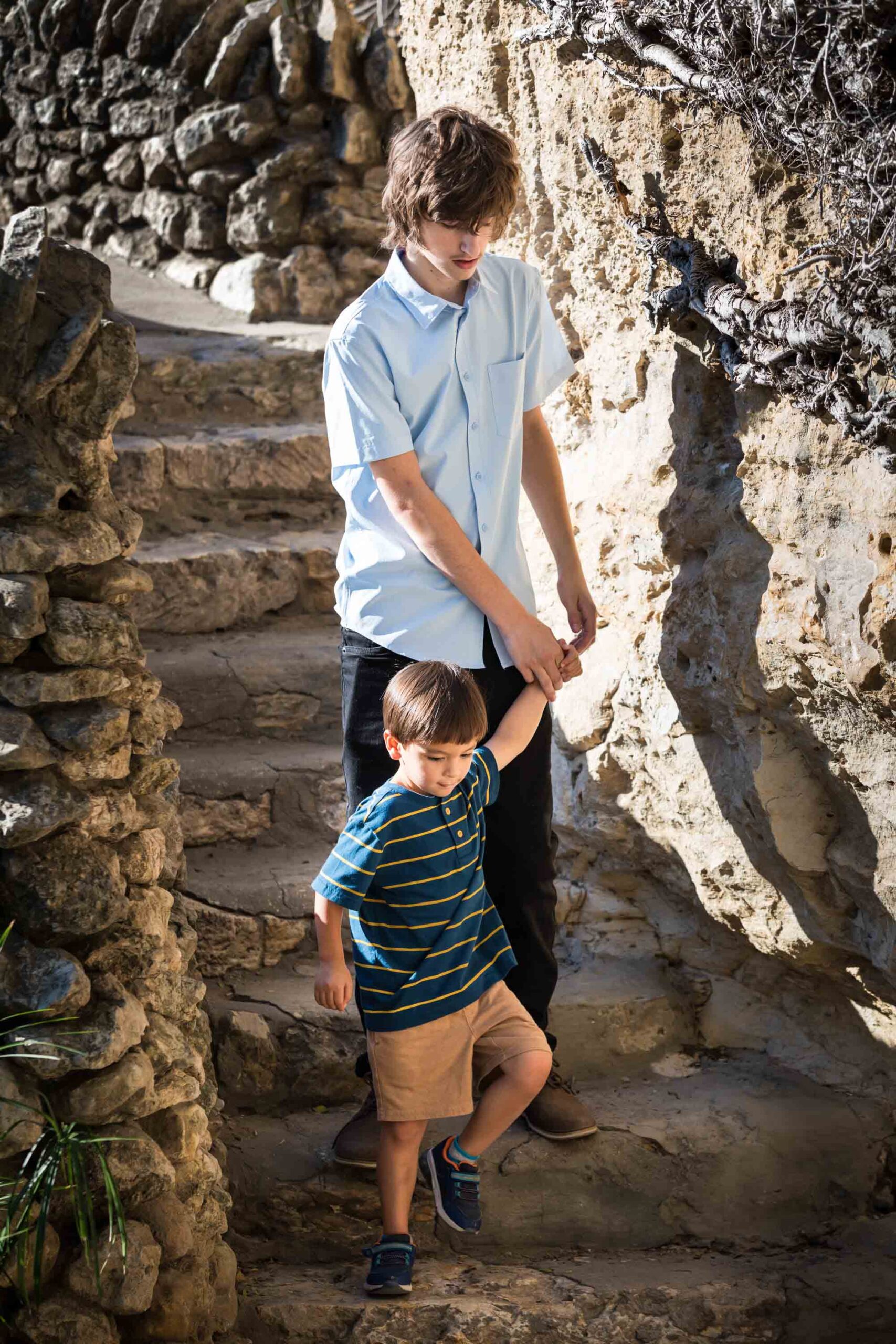 Little boy and teenage brother walking down stone steps holding hands