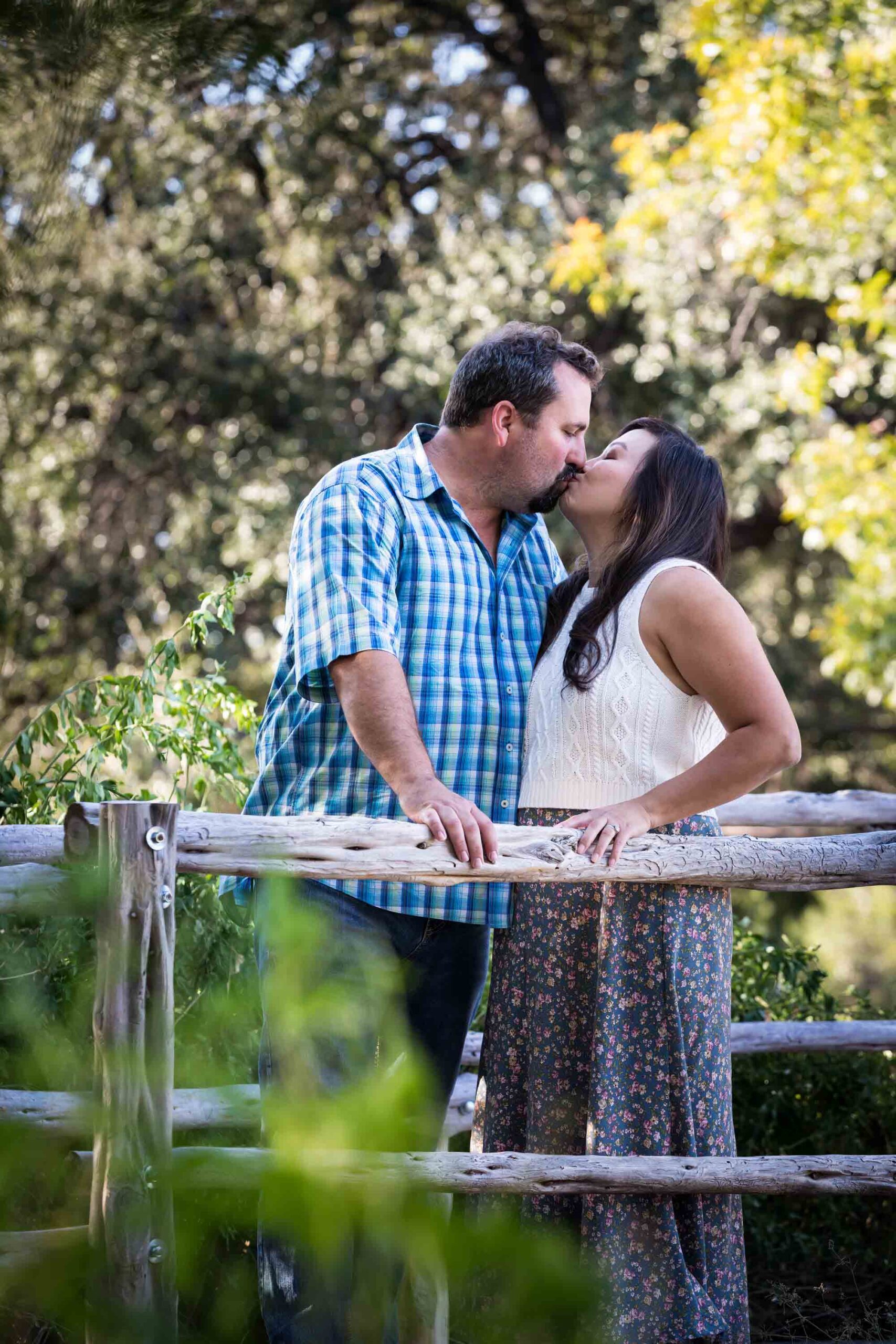 Parents kissing on wooden bridge with trees in the background for an article on photo tips for families with young children