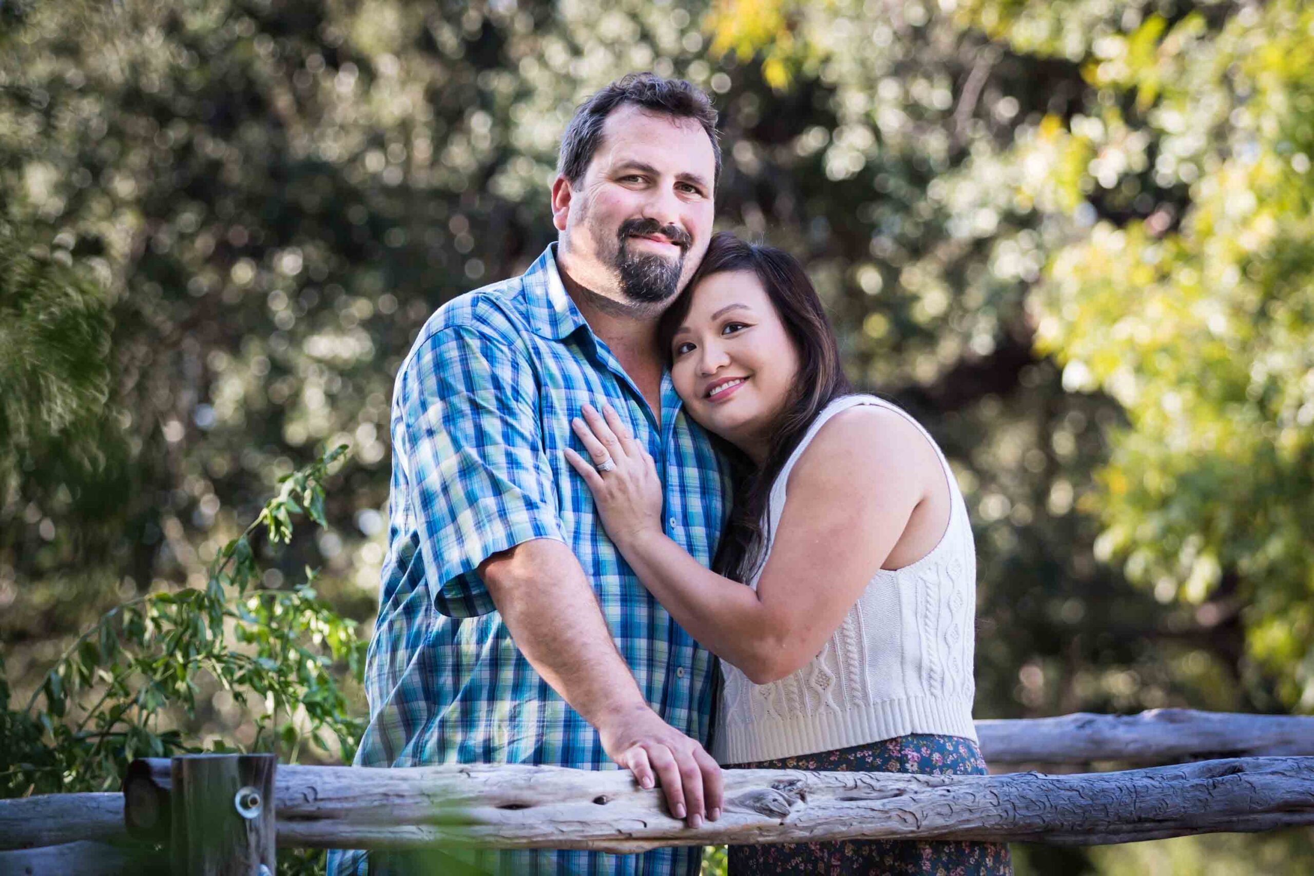 Parents hugging on wooden bridge with trees in the background for an article on photo tips for families with young children