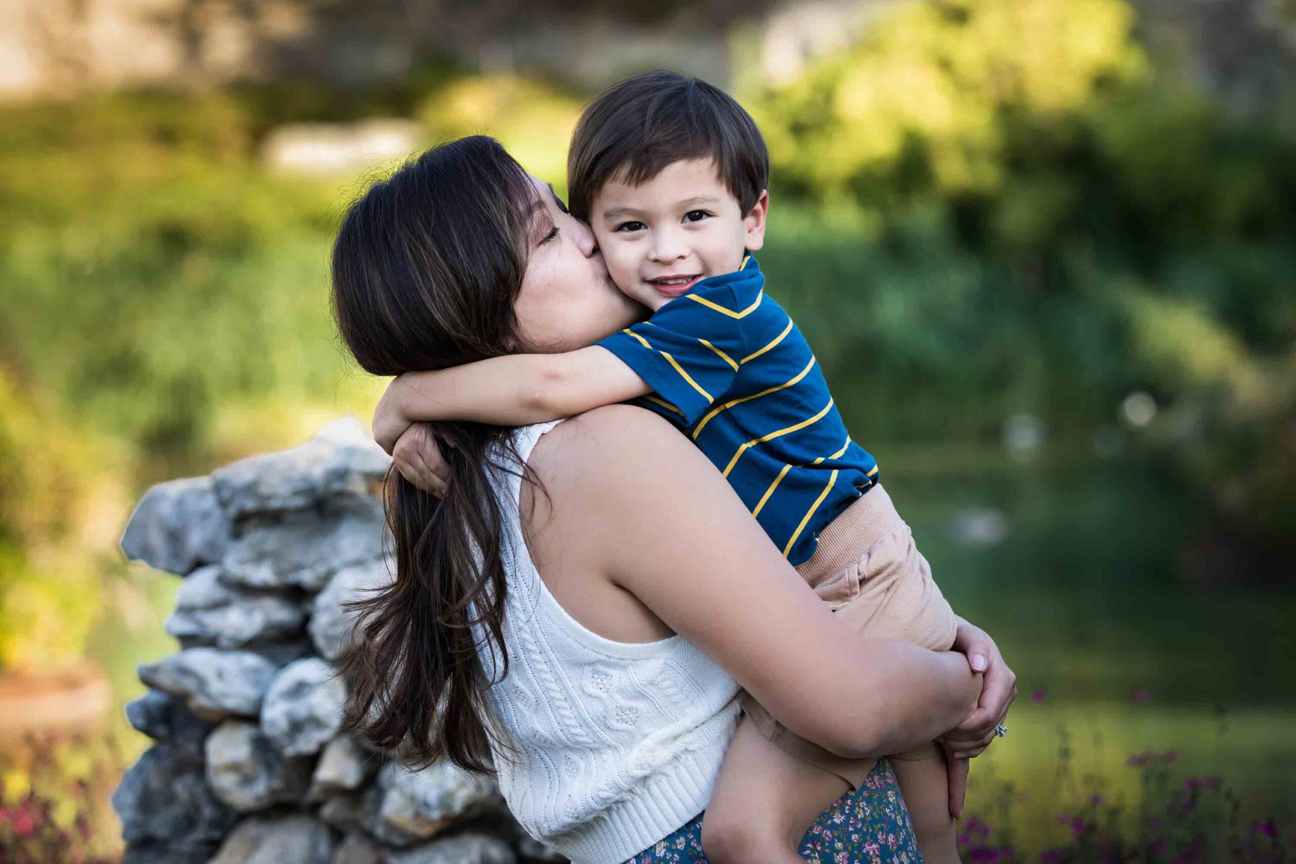 Mother hugging little boy with brown hair wearing striped shirt for an article on photo tips for families with young children