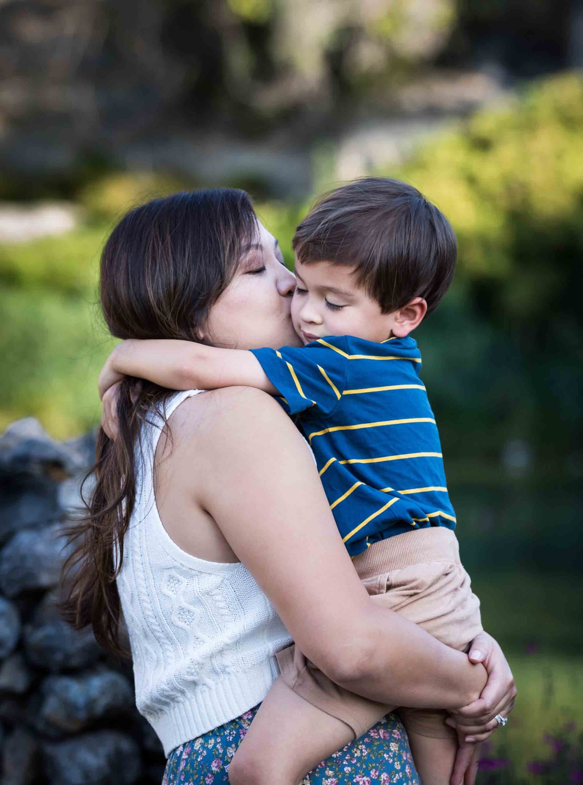 Mother kissing and hugging little boy with brown hair wearing striped shirt for an article on photo tips for families with young children