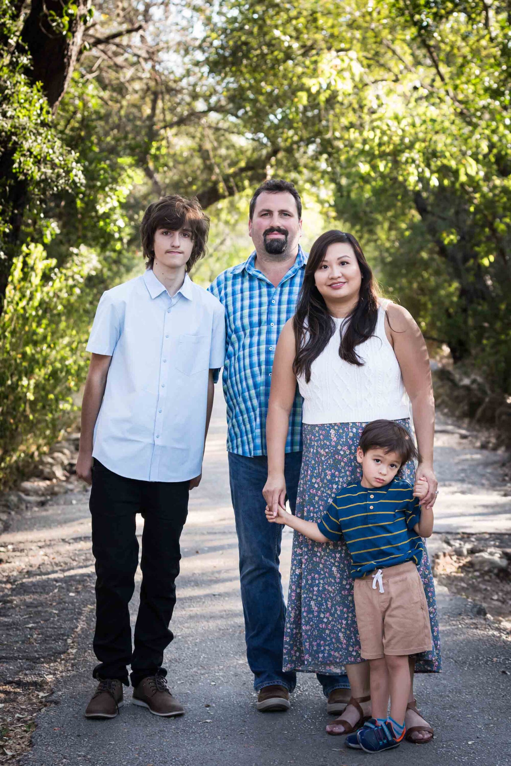 Parents with teenager boy and young boy standing in pathway in forested park for an article on photo tips for families with young children