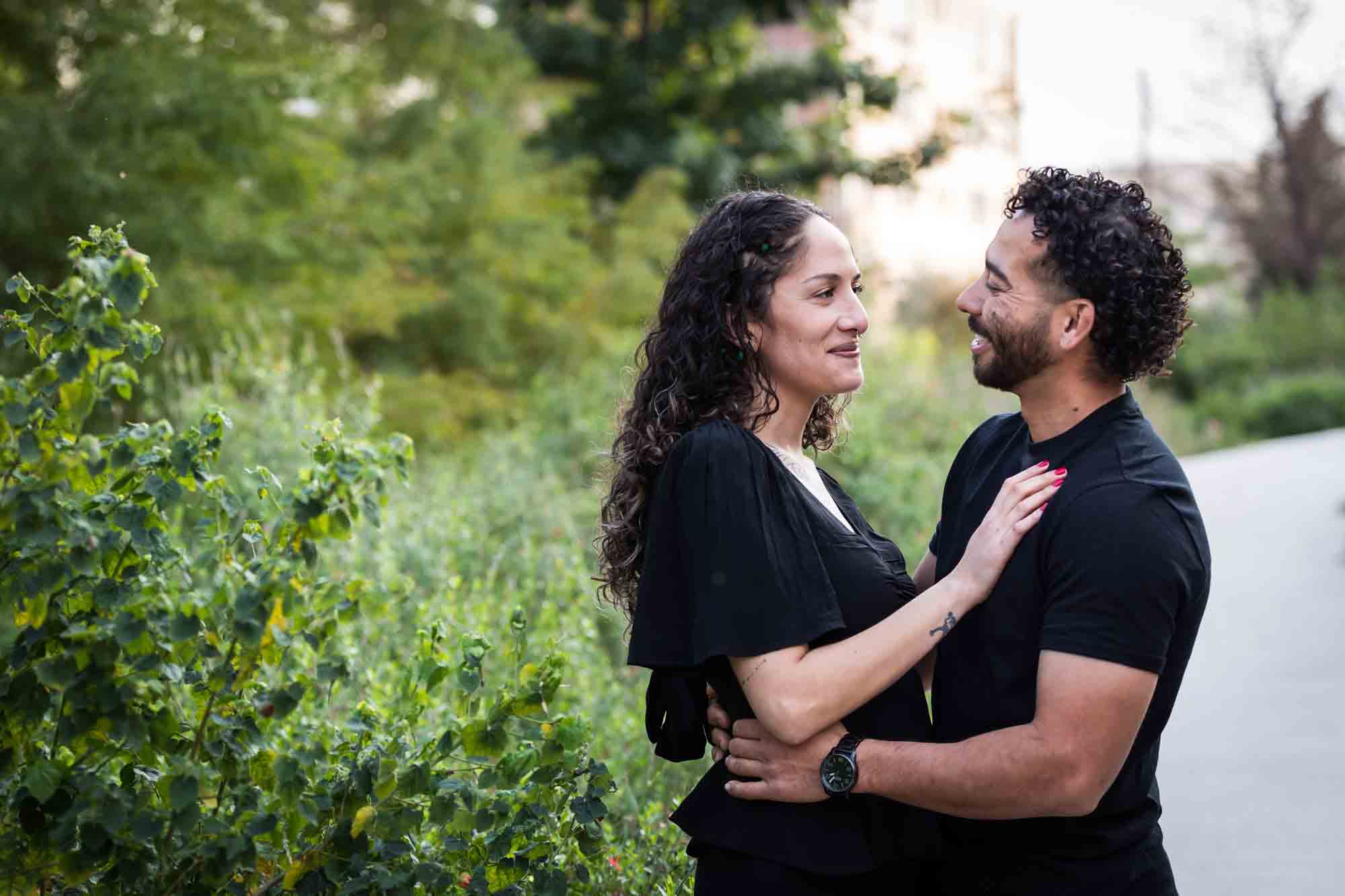 Couple wearing black t-shirts hugging in front of green bushes during a San Pedro Creek Park family portrait session