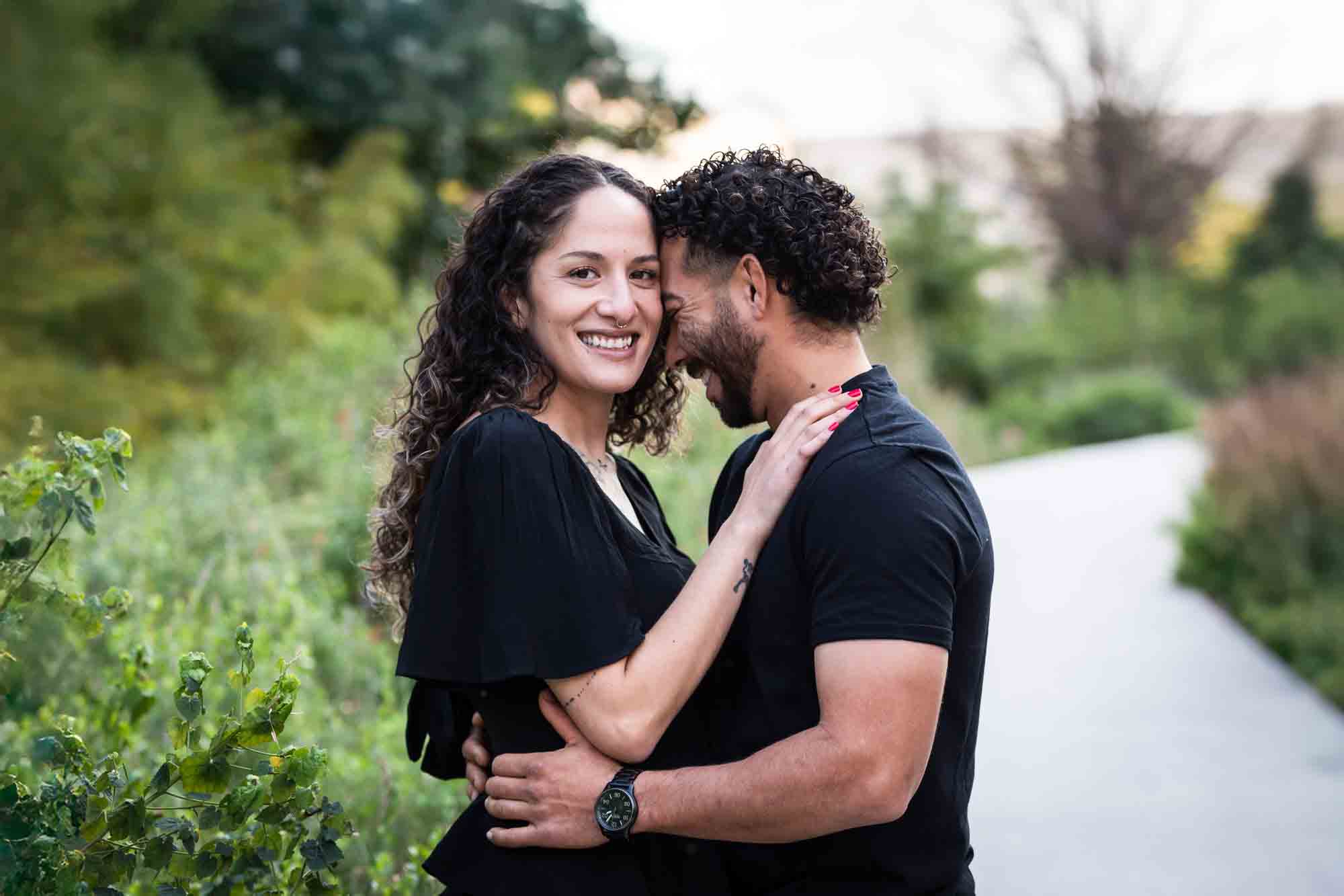 Couple wearing black t-shirts hugging in front of green bushes during a San Pedro Creek Park family portrait session