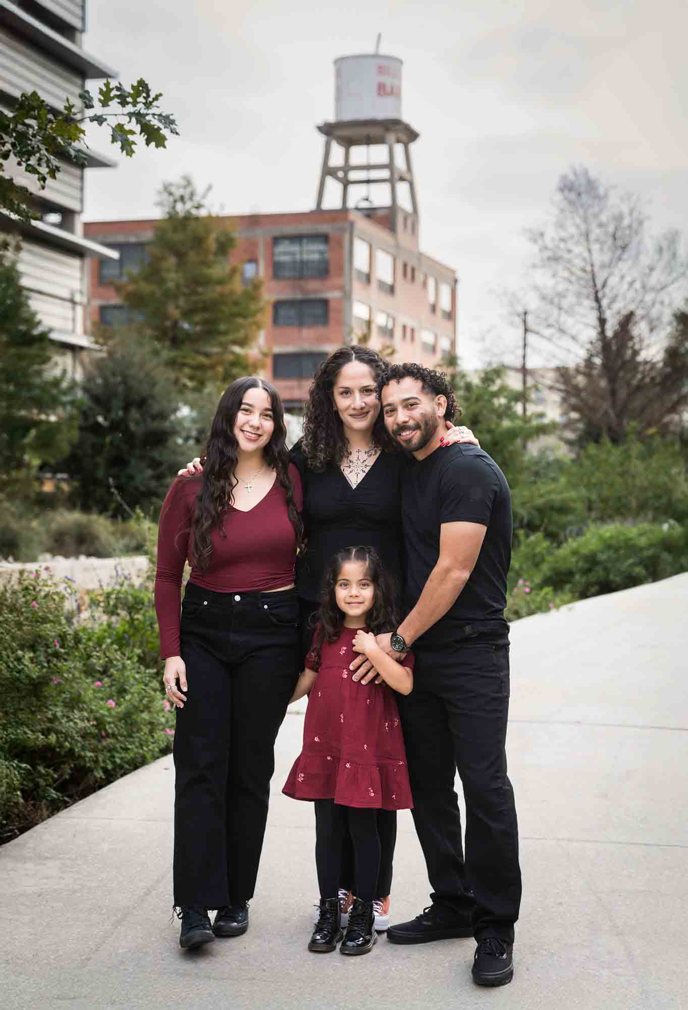 Family of parents, teen girl, and little girl hugging on sidewalk during a San Pedro Creek Park family portrait session