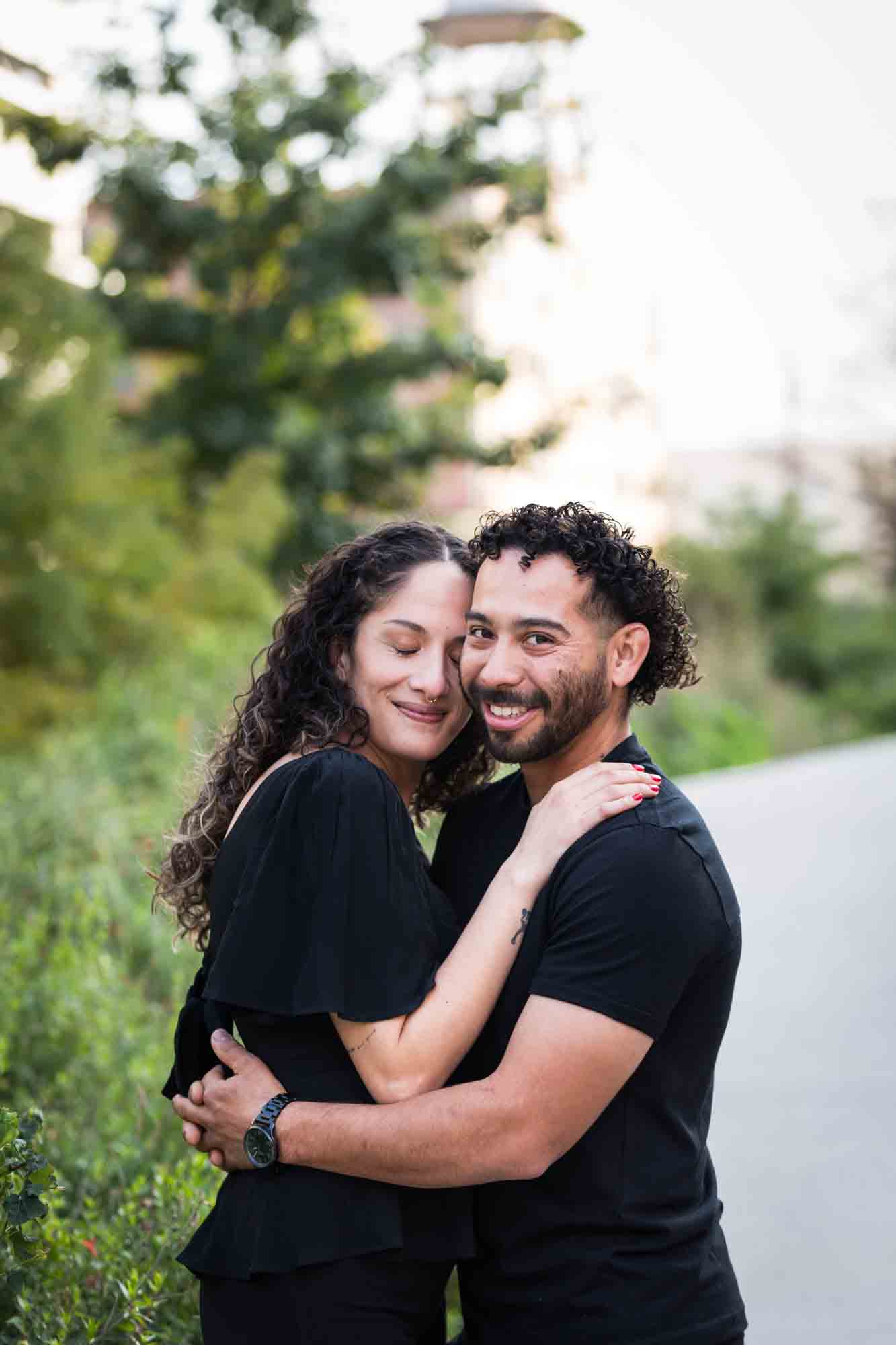 Couple wearing black t-shirts hugging in front of green bushes during a San Pedro Creek Park family portrait session