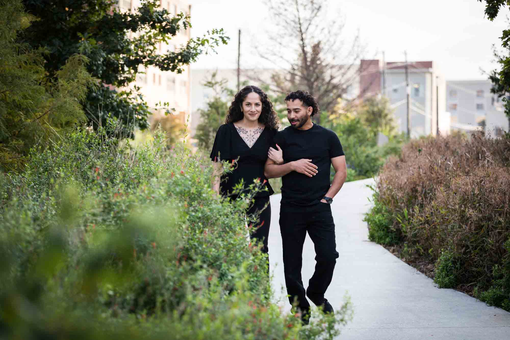 Couple wearing black t-shirts walking in front of green bushes during a San Pedro Creek Park family portrait session