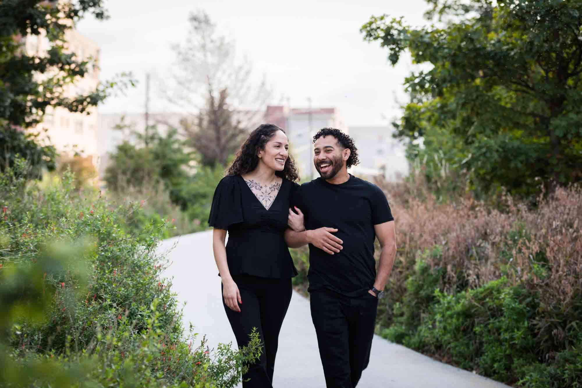 Couple wearing black t-shirts walking in front of green bushes during a San Pedro Creek Park family portrait session