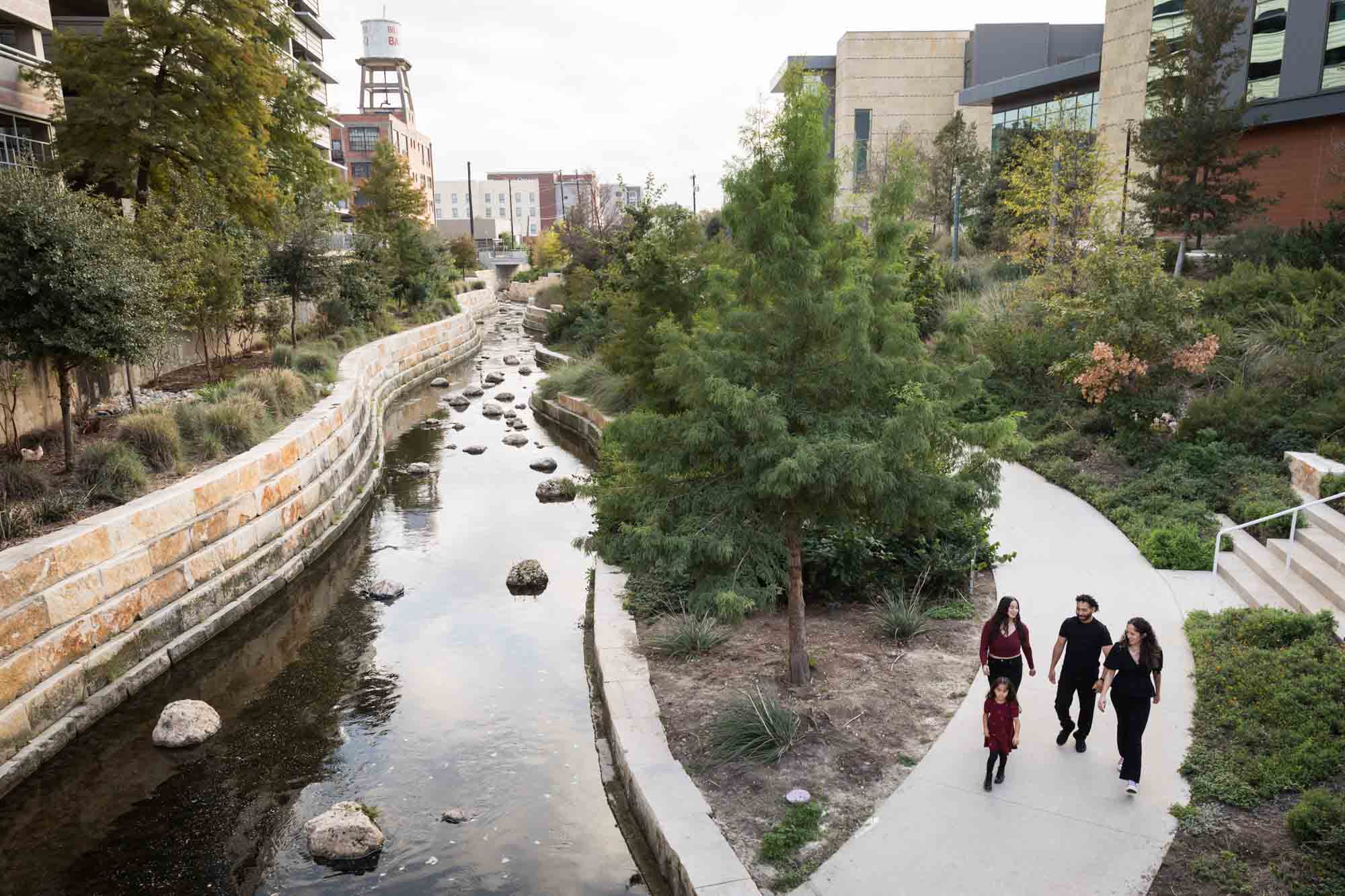 Family of two parents, teen girl, and little girl walking along pathway beside San Pedro Creek during a San Pedro Creek Park family portrait session