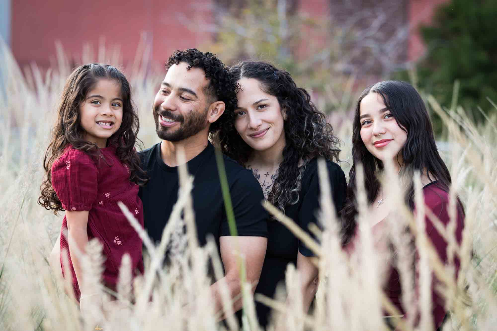 Family of two parents, teen girl, and little girl posed behind wheat-like bushes during a San Pedro Creek Park family portrait session